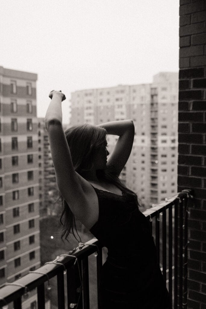 Woman leaning backwards off balcony with arms up in moody B&W photo