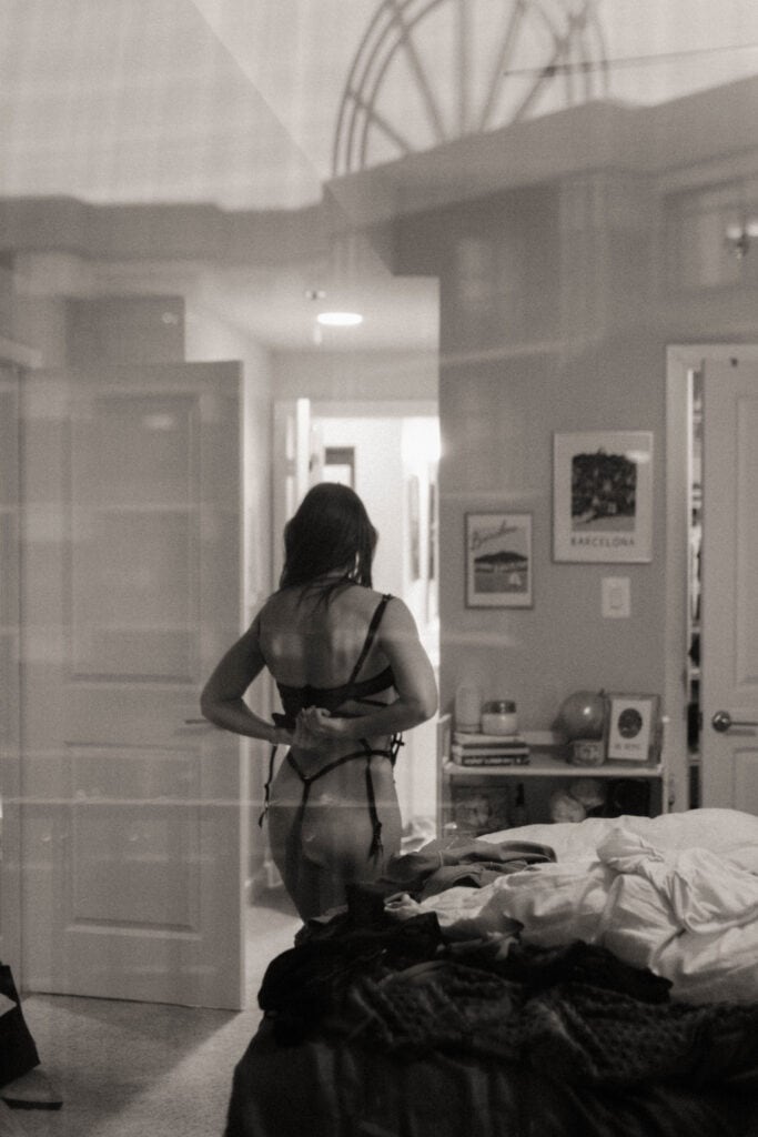 Woman seen undressing through glass in B&W bedroom photo