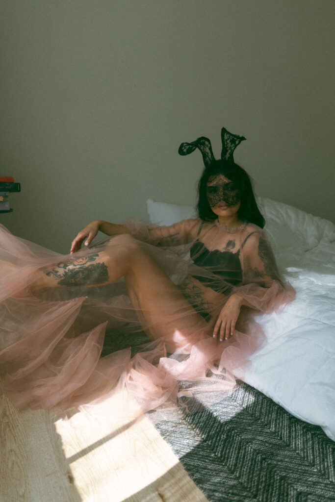 a woman posing in bed with a lace mask and ears and tulle shear dress at her boudoir session 
