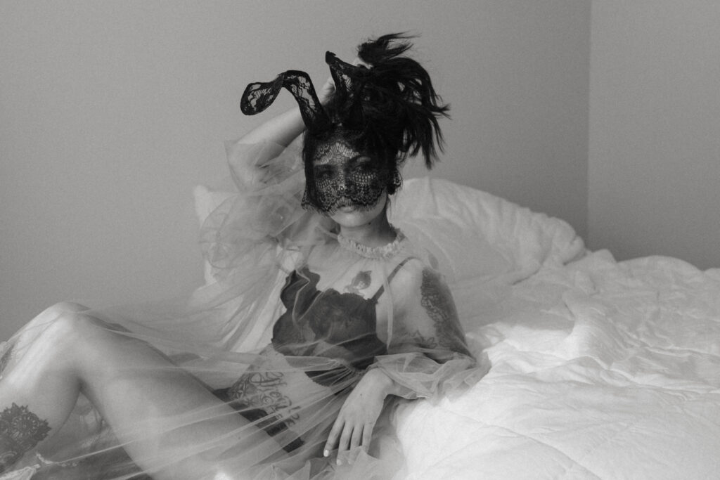 a woman posing against bed with a lace mask and ears and tulle shear dress at her boudoir session 