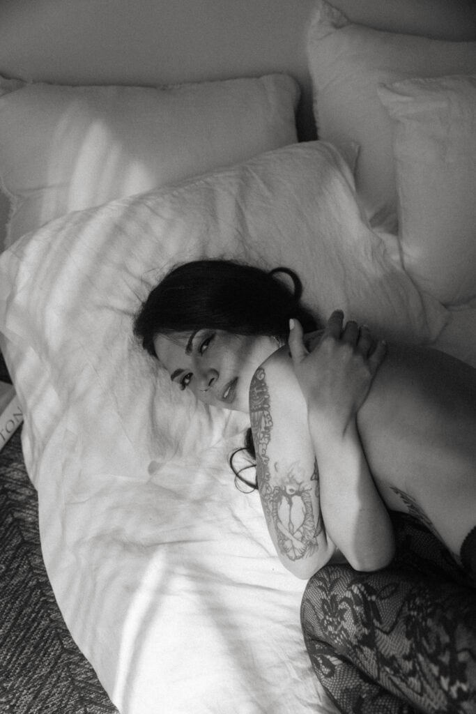a woman hugging herself in a bed with black lace tights