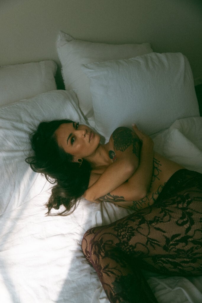a woman in a bed with black lace tights on during her boudoir session