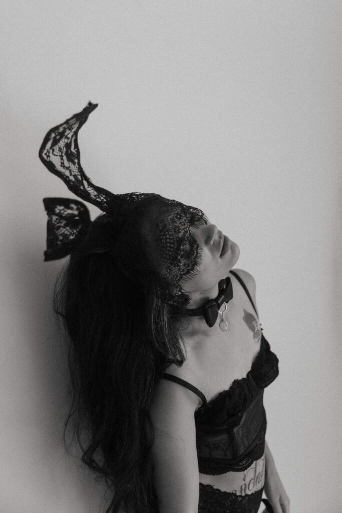 a woman standing against a wall with a black lace mask and ears on during her boudoir session 