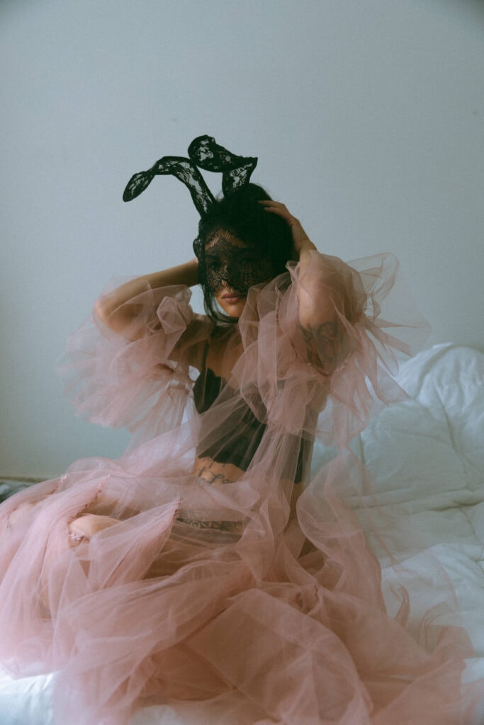 a woman with a lace mask and ears and tulle shear dress at her boudoir session 