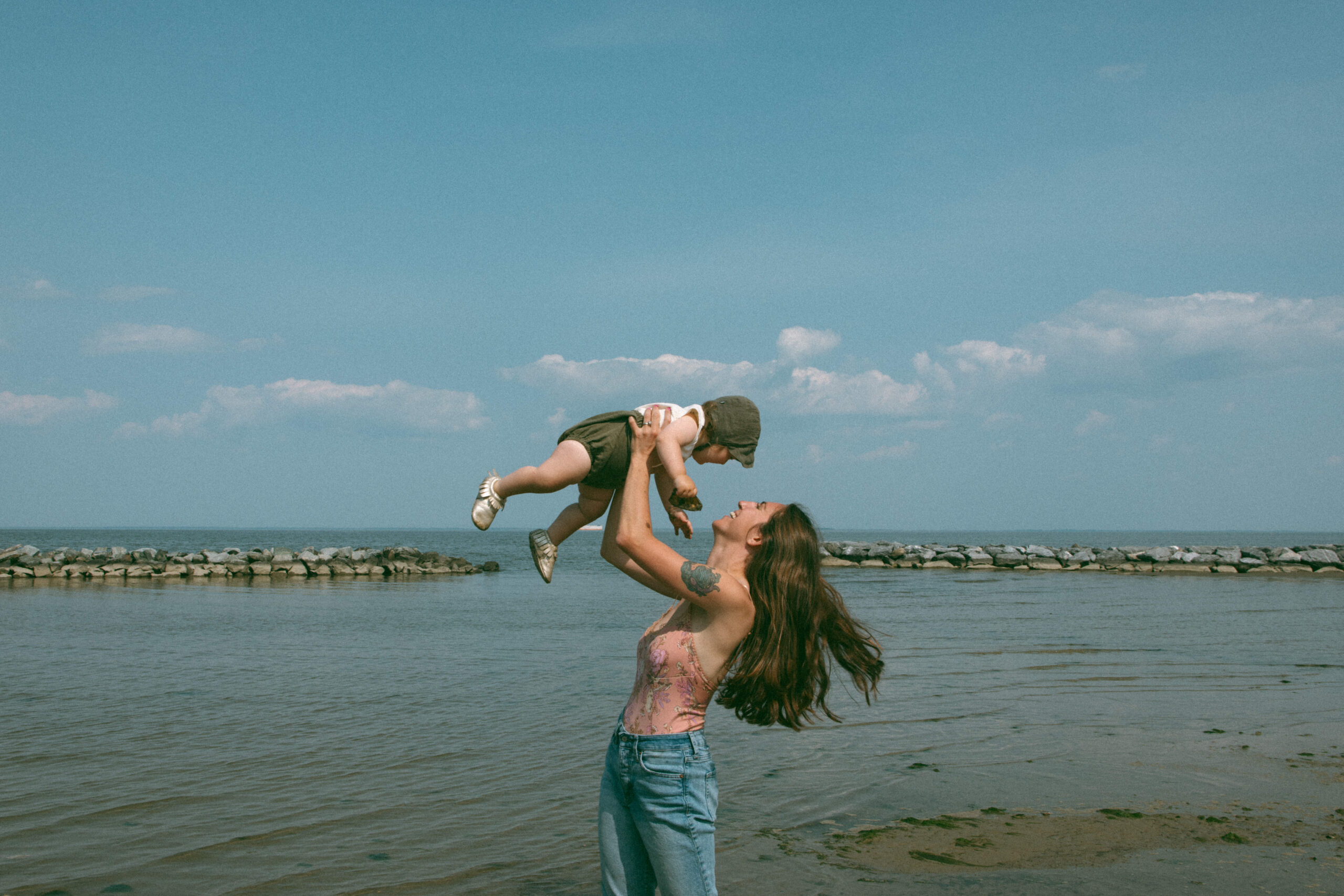 mother holding daughter up in the air on the beach during motherhood photoshoot 