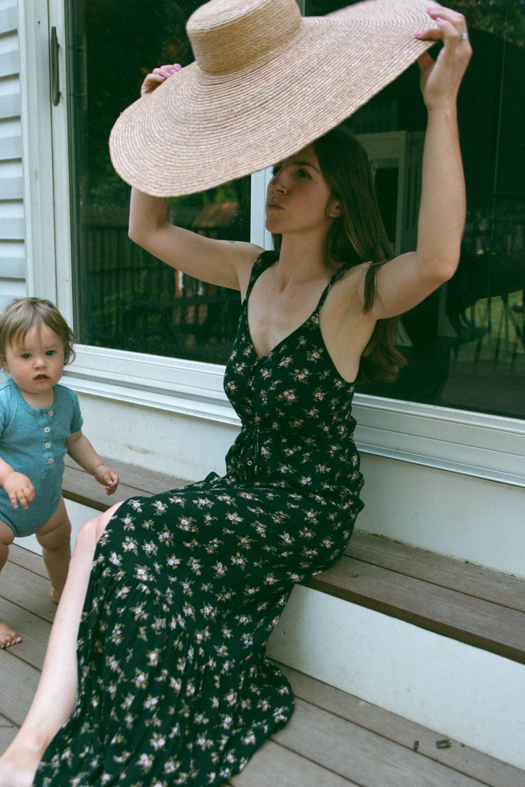mother putting on large sunhat while sitting on the steps with her baby 