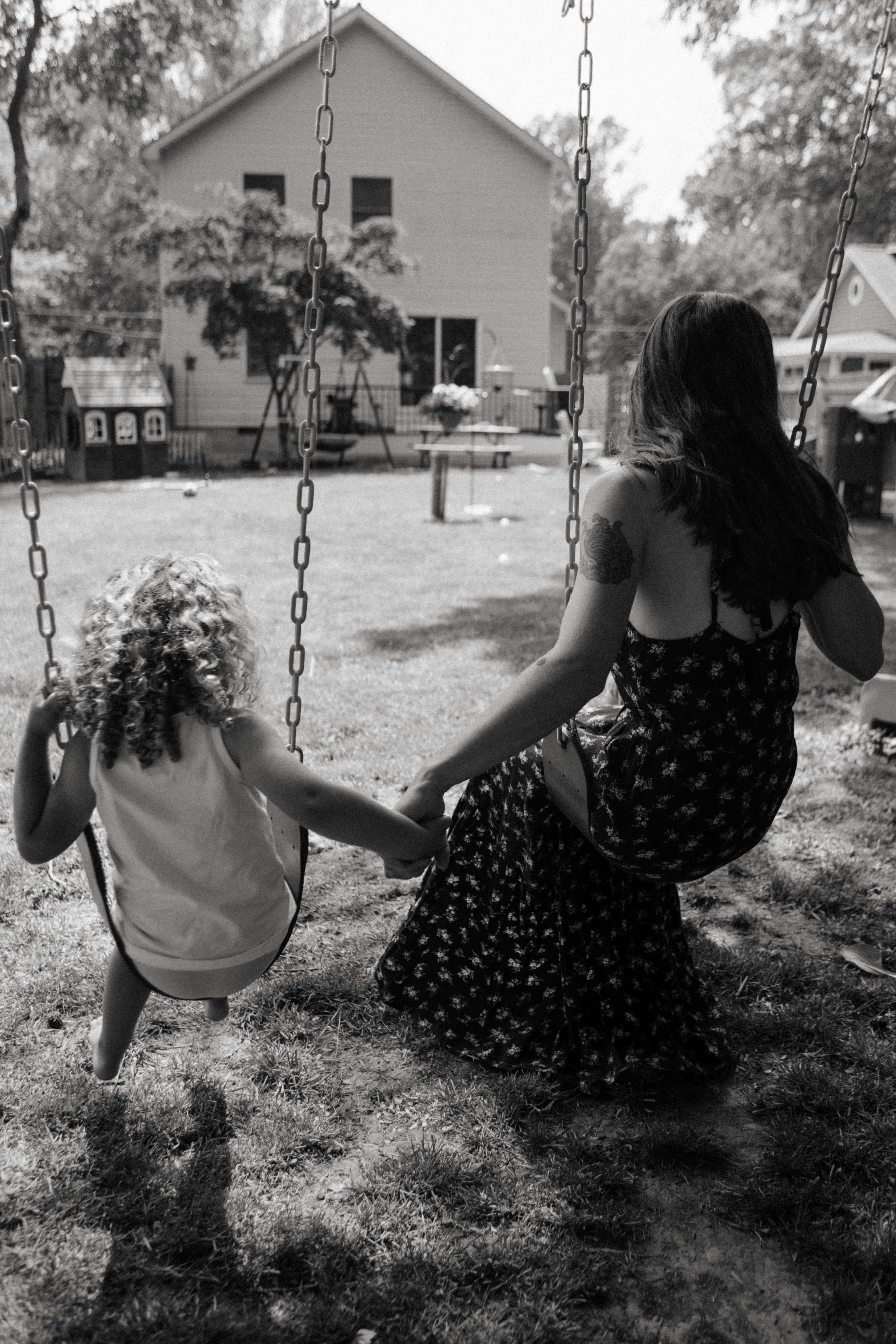 black and white shot from the back of mother and son holding hands and swinging 
