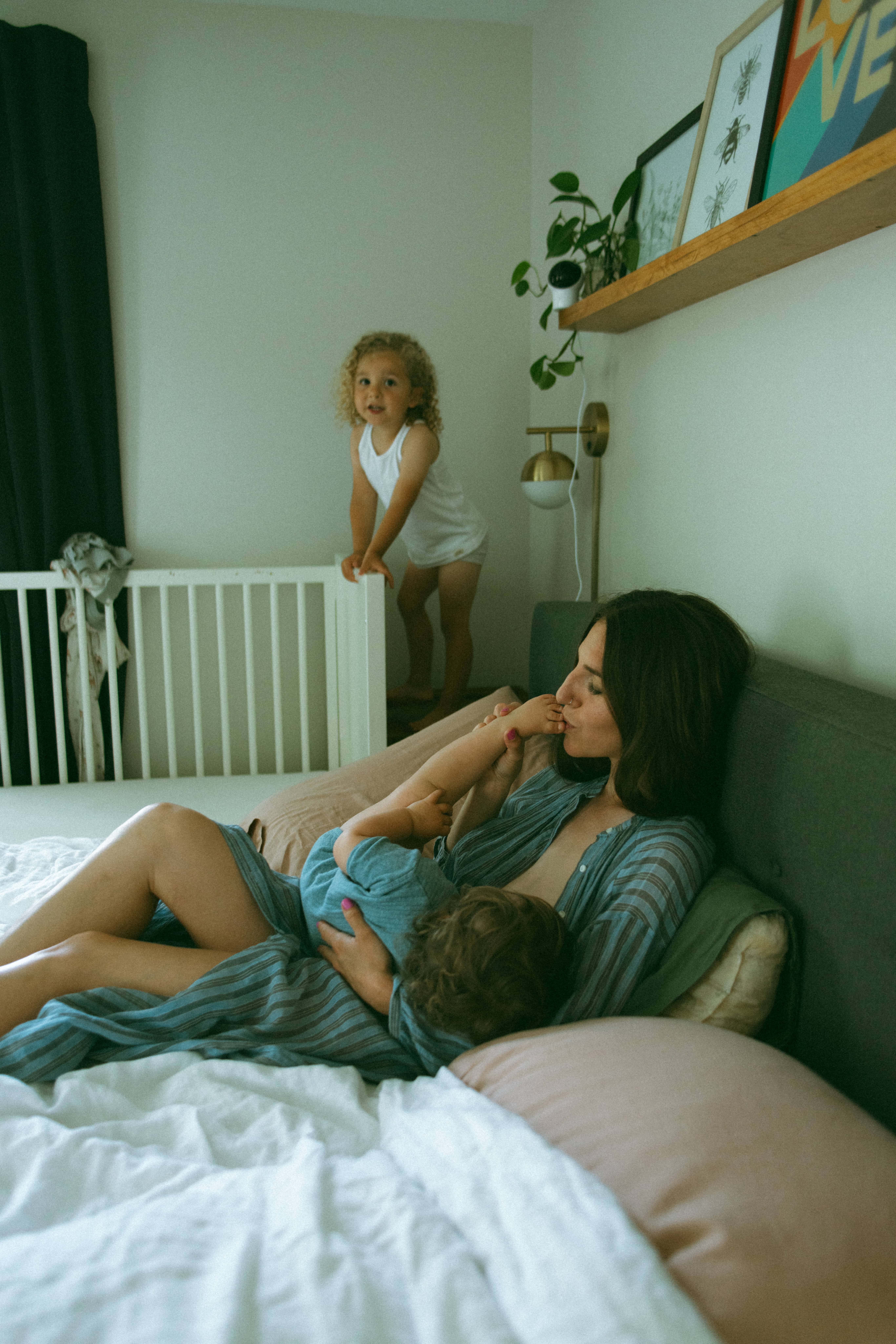 mother breastfeeding and kissing daughters feet and son playing 