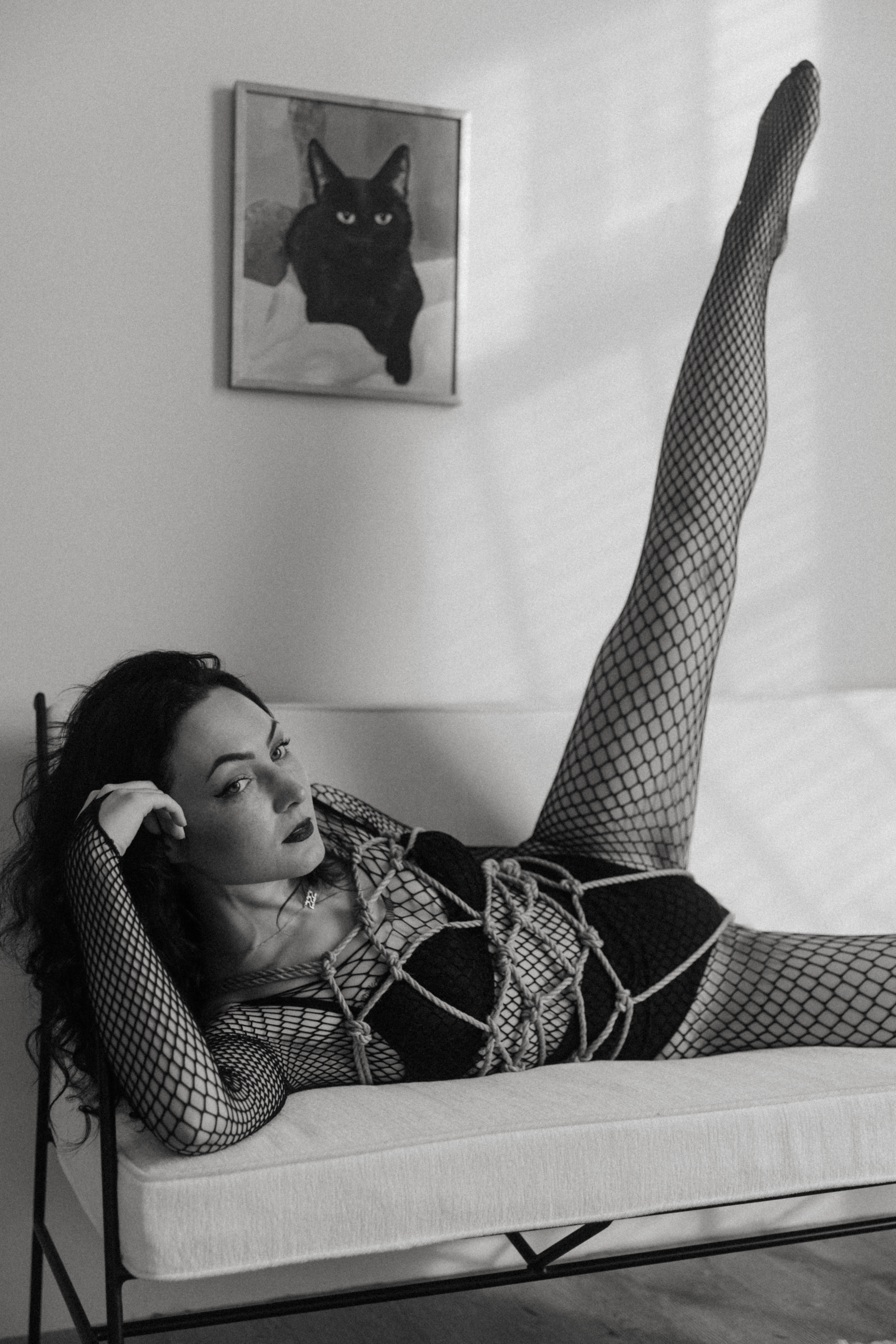 black and white photo of woman in fishnet body suit and sensual shibari ropes tied around torso
