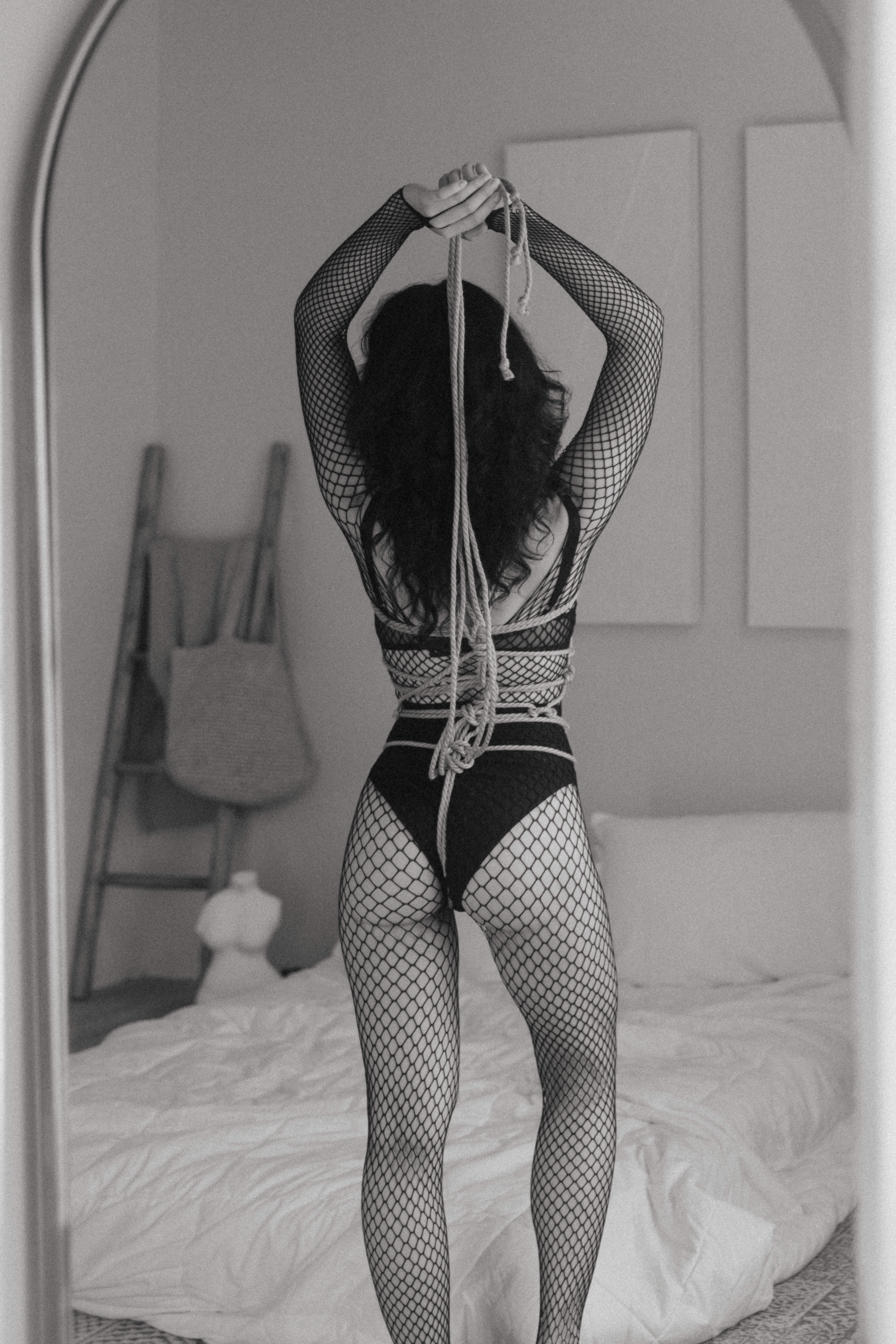 black and white of a woman in fishnets holding the rope above her head that's tied around her body 