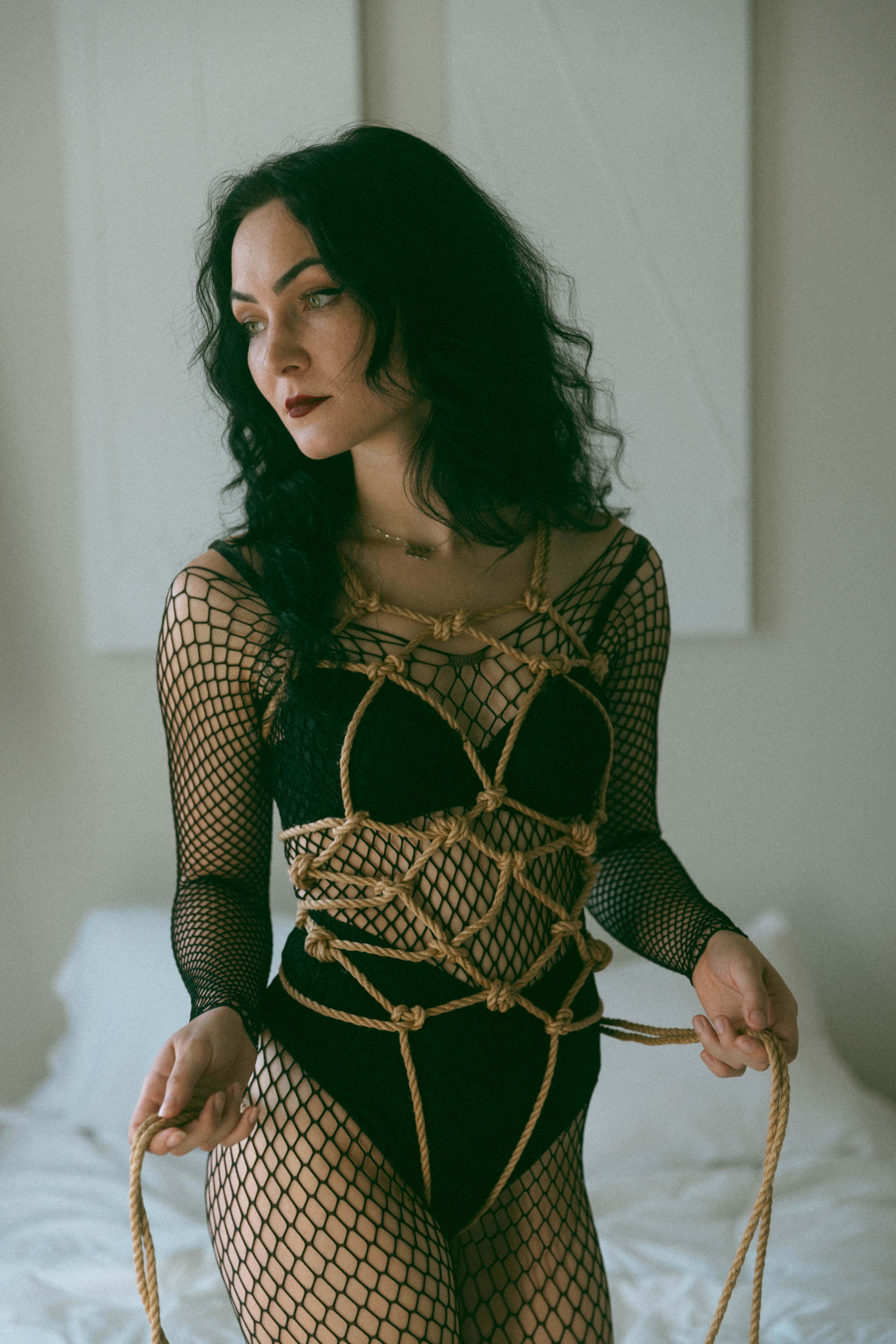 a woman in a fish net body suit with ropes tied around her torso during a sensual shibari session