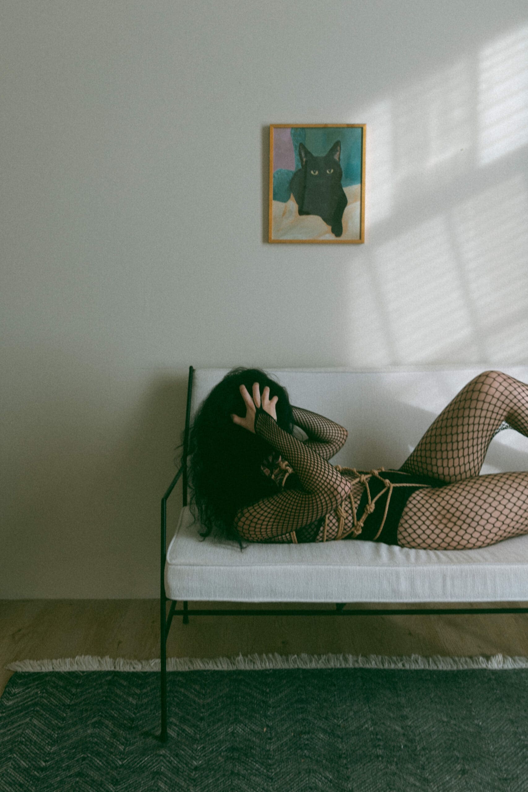 a woman in a fishnet bodysuit laying on a couch with shibari ropes tied around her whole torso