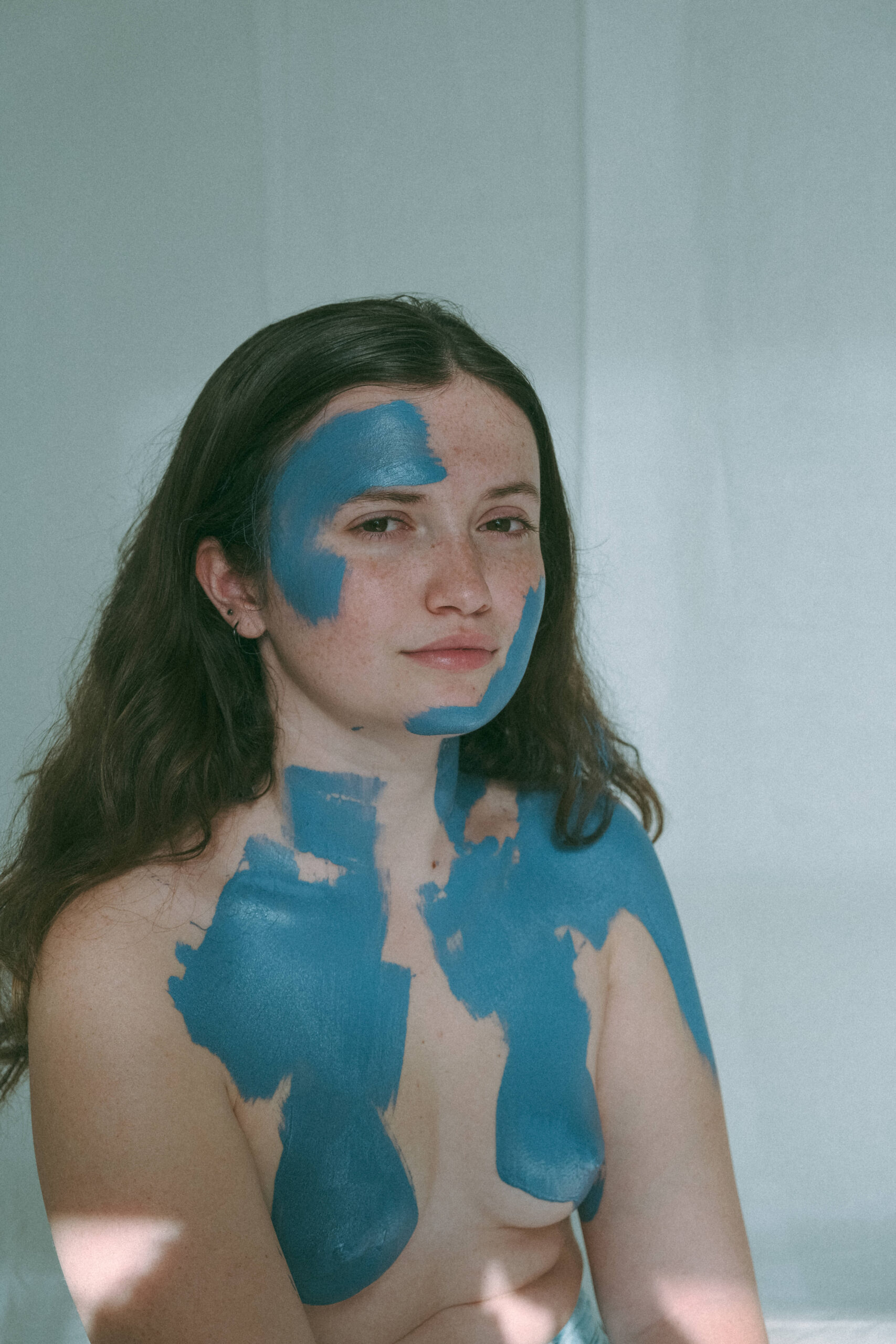 model during a creative model photoshoot, topless with blue paint on her body 