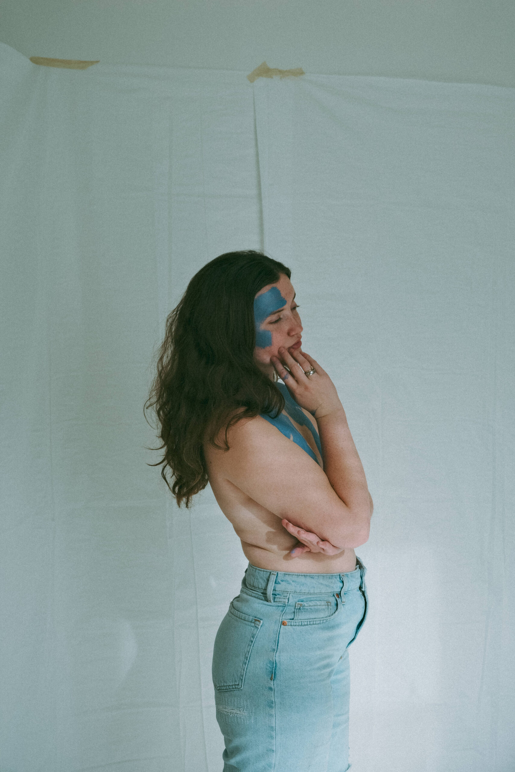 woman standing topless with her arms across her chest and blue paint on her body