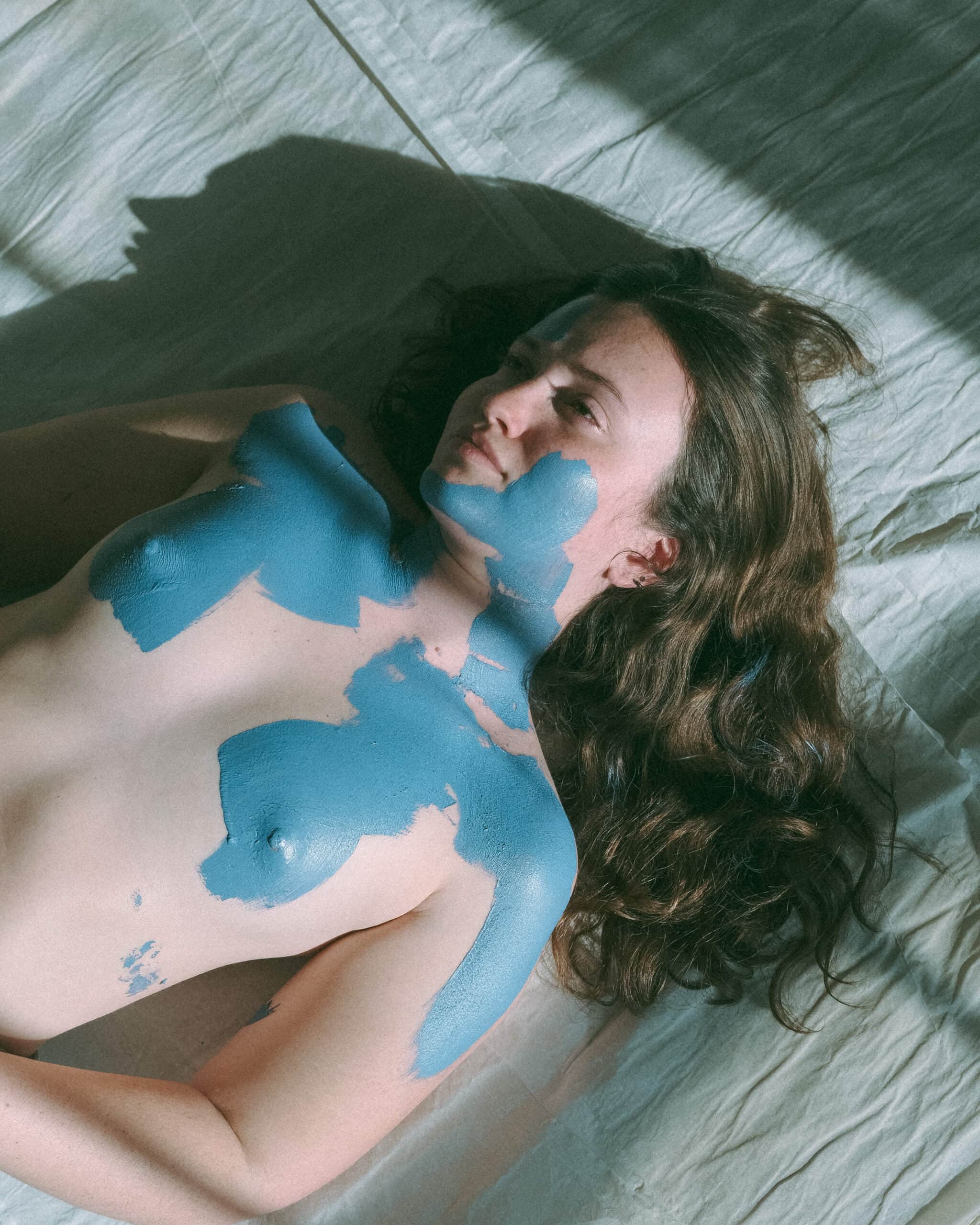 a woman during a creative model photoshoot laying on the ground painted blue