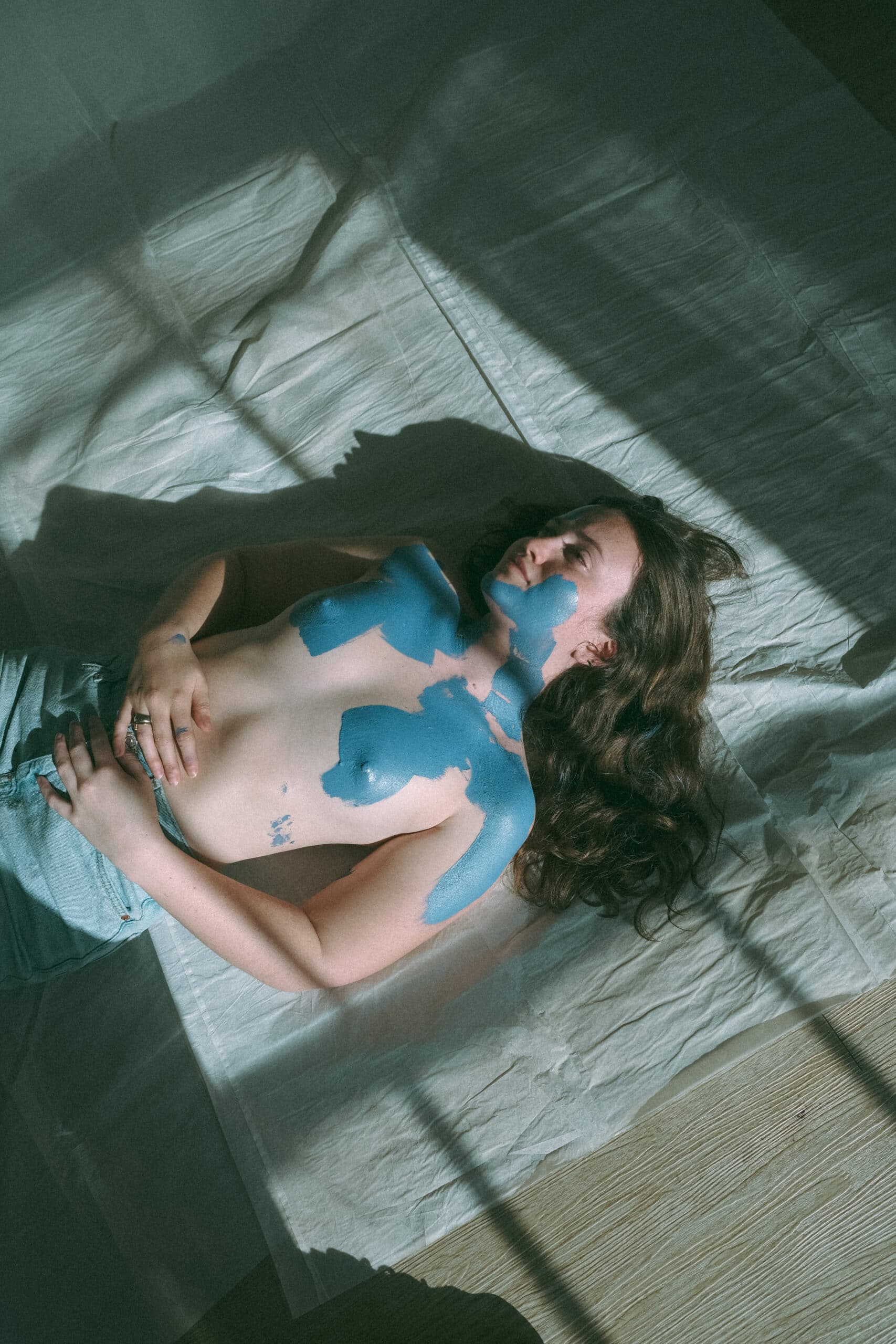 topless woman during a creative model photoshoot laying on the floor with shadows on her painted body