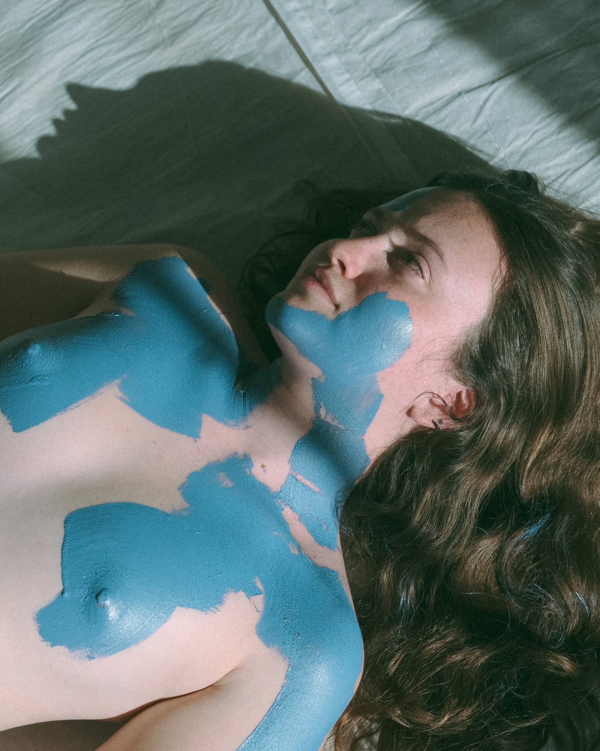 woman during a creative model photoshoot laying down with blue paint on her body 