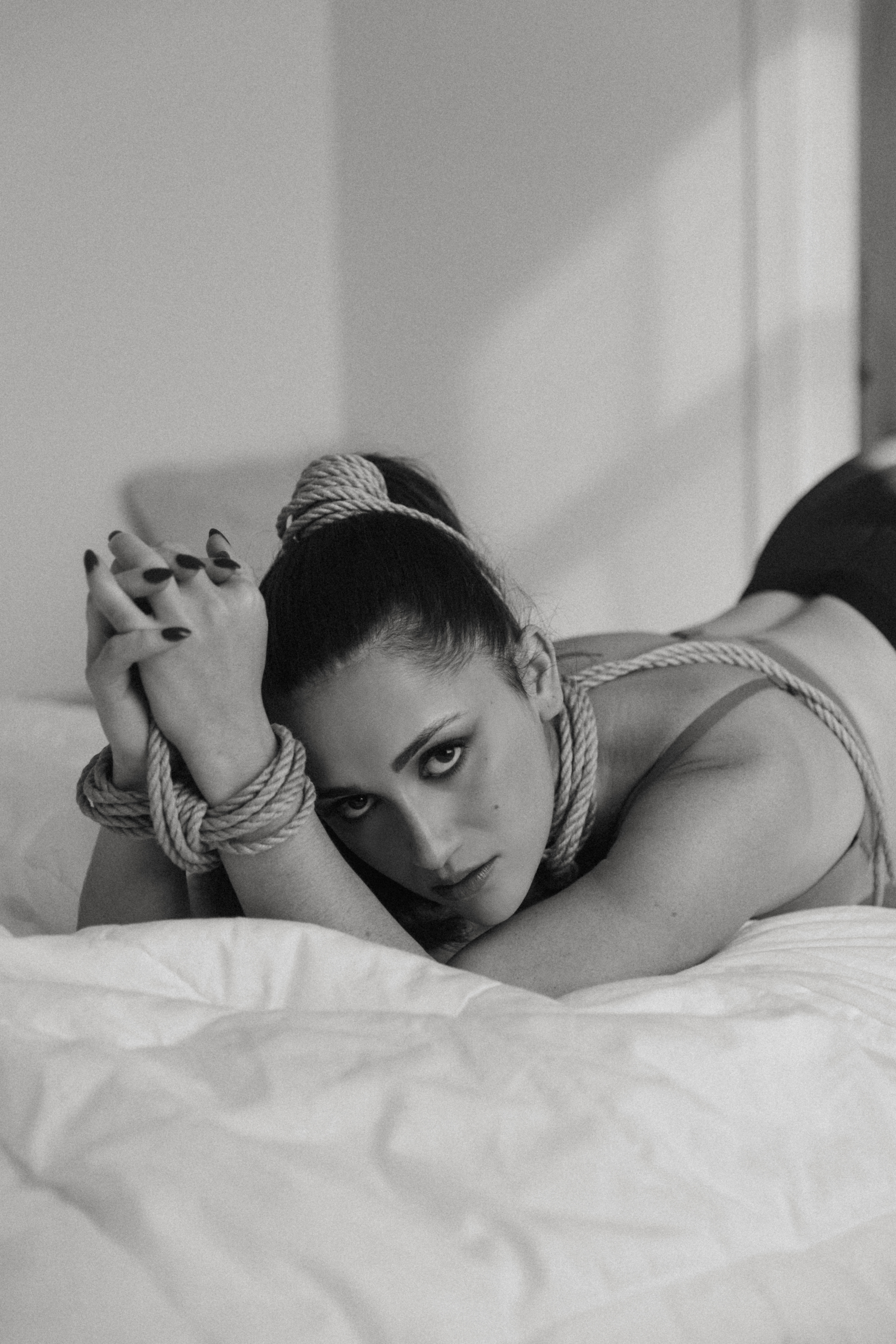black and white of a woman tied up on a bed with a fierce look on her face