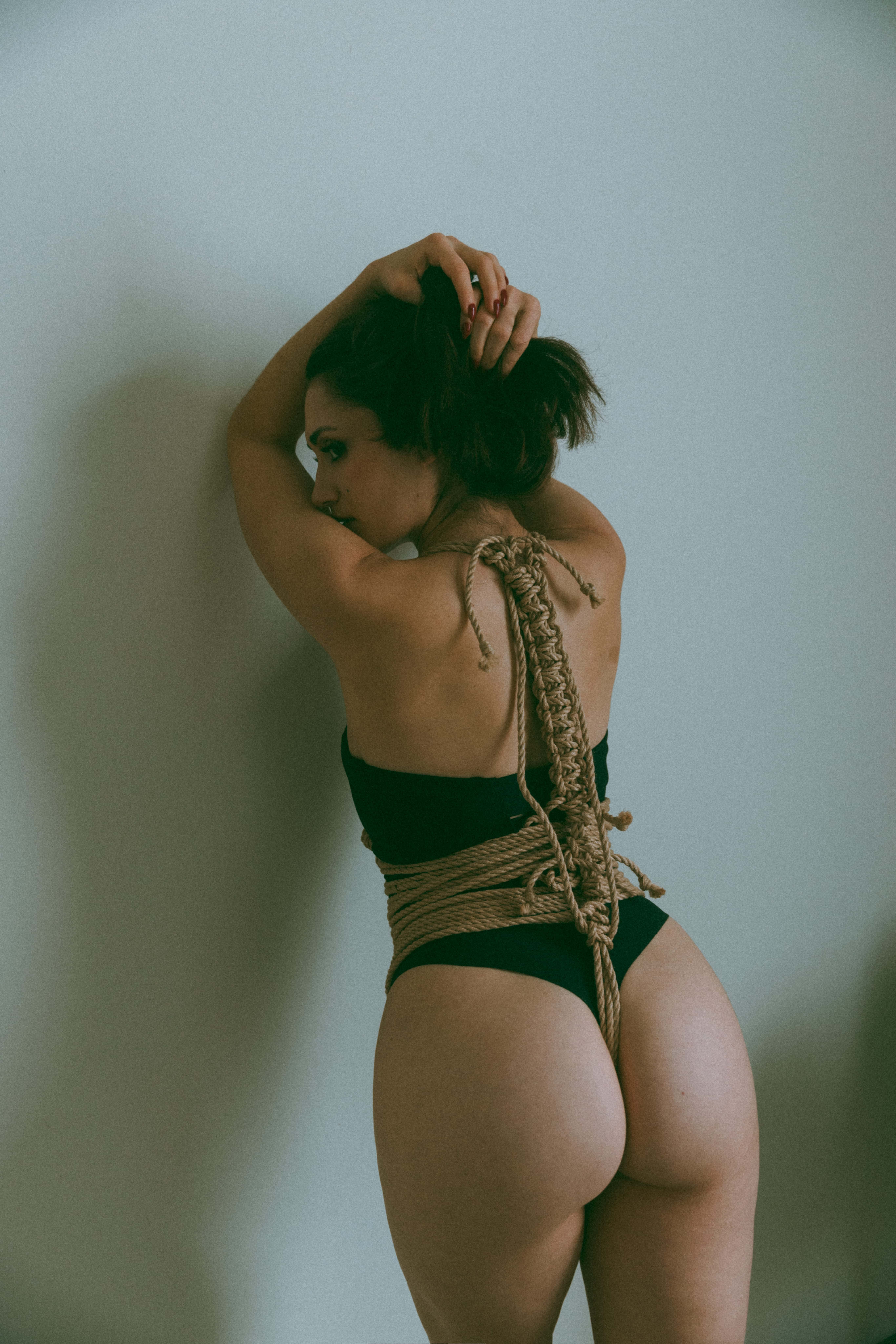 the back side of a woman leaning against a wall with ropes tied around her waist and torso