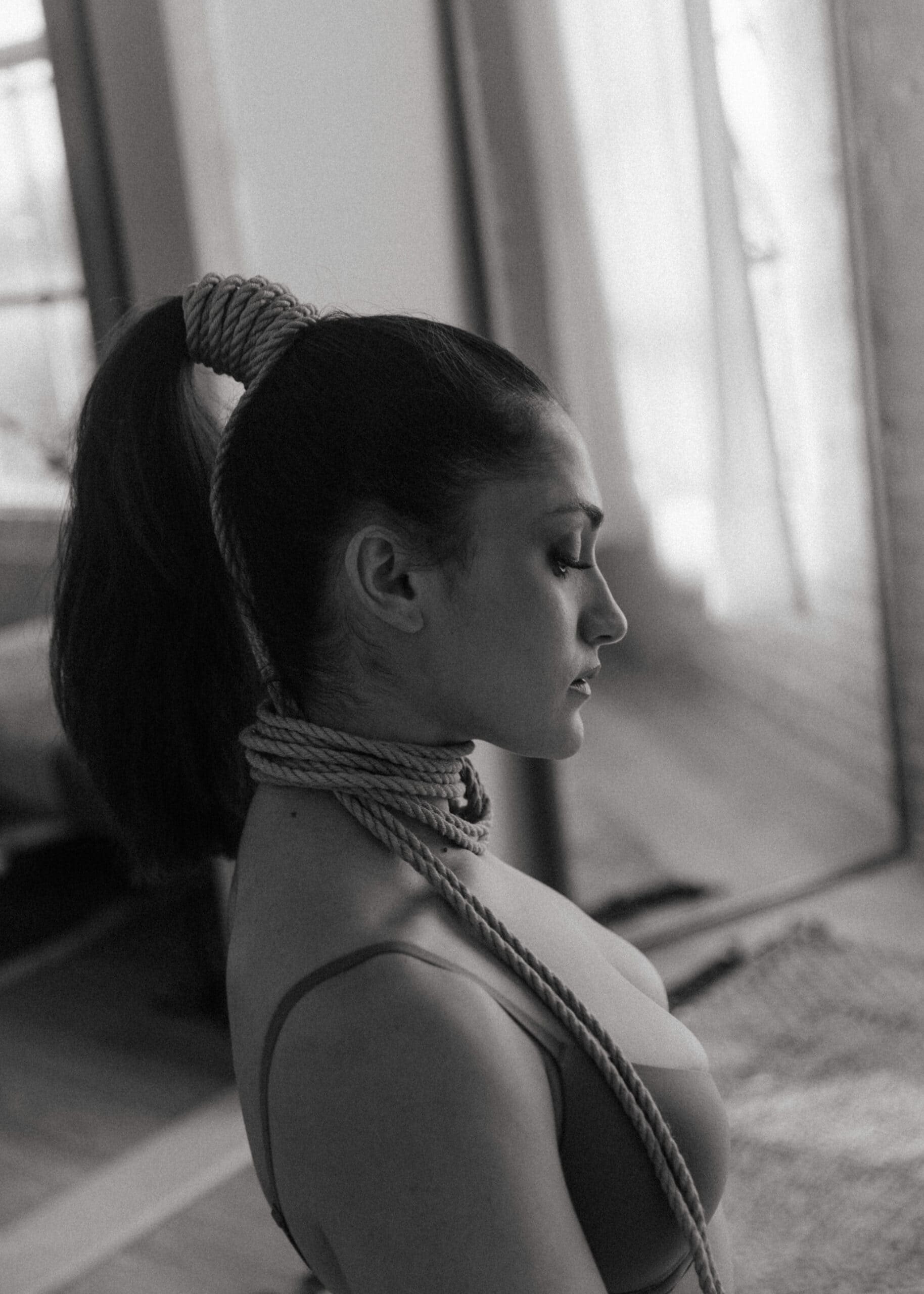 black and white of a woman with ropes tied around her neck and ponytail