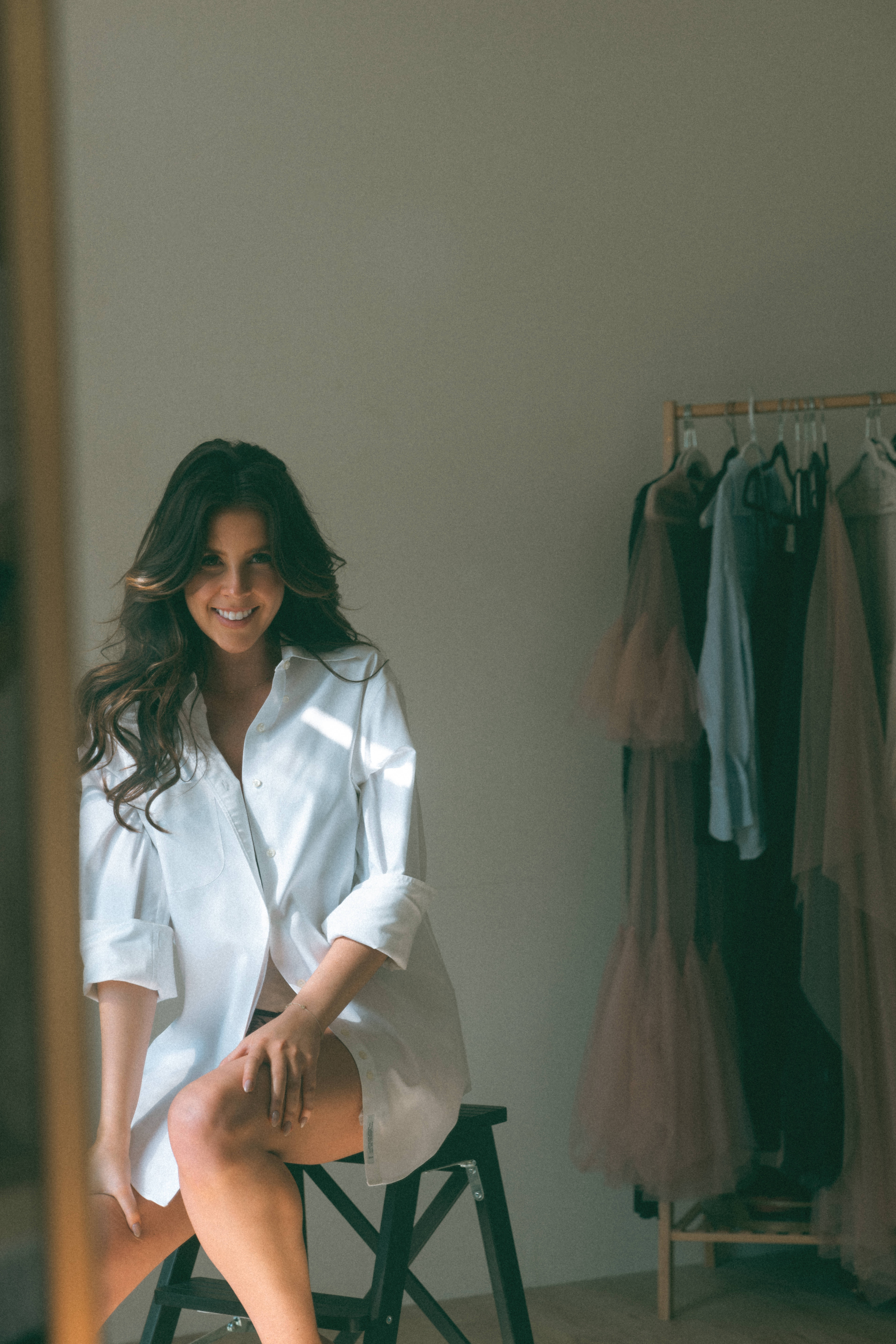 a woman sitting and smiling while wearing a white oversized shirt during a boudoir session 