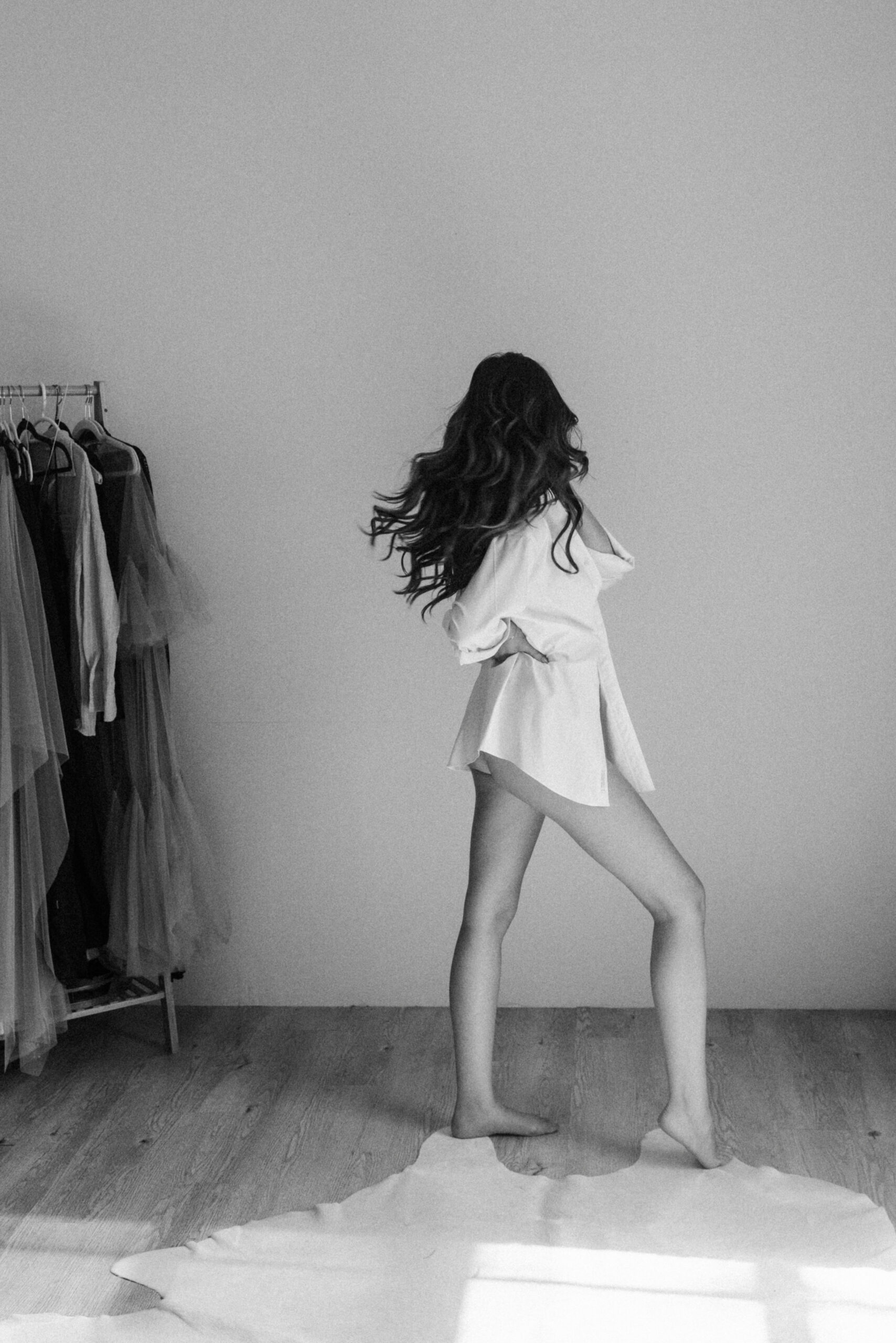 a woman standing in a oversized white shirt and flipping her hair 