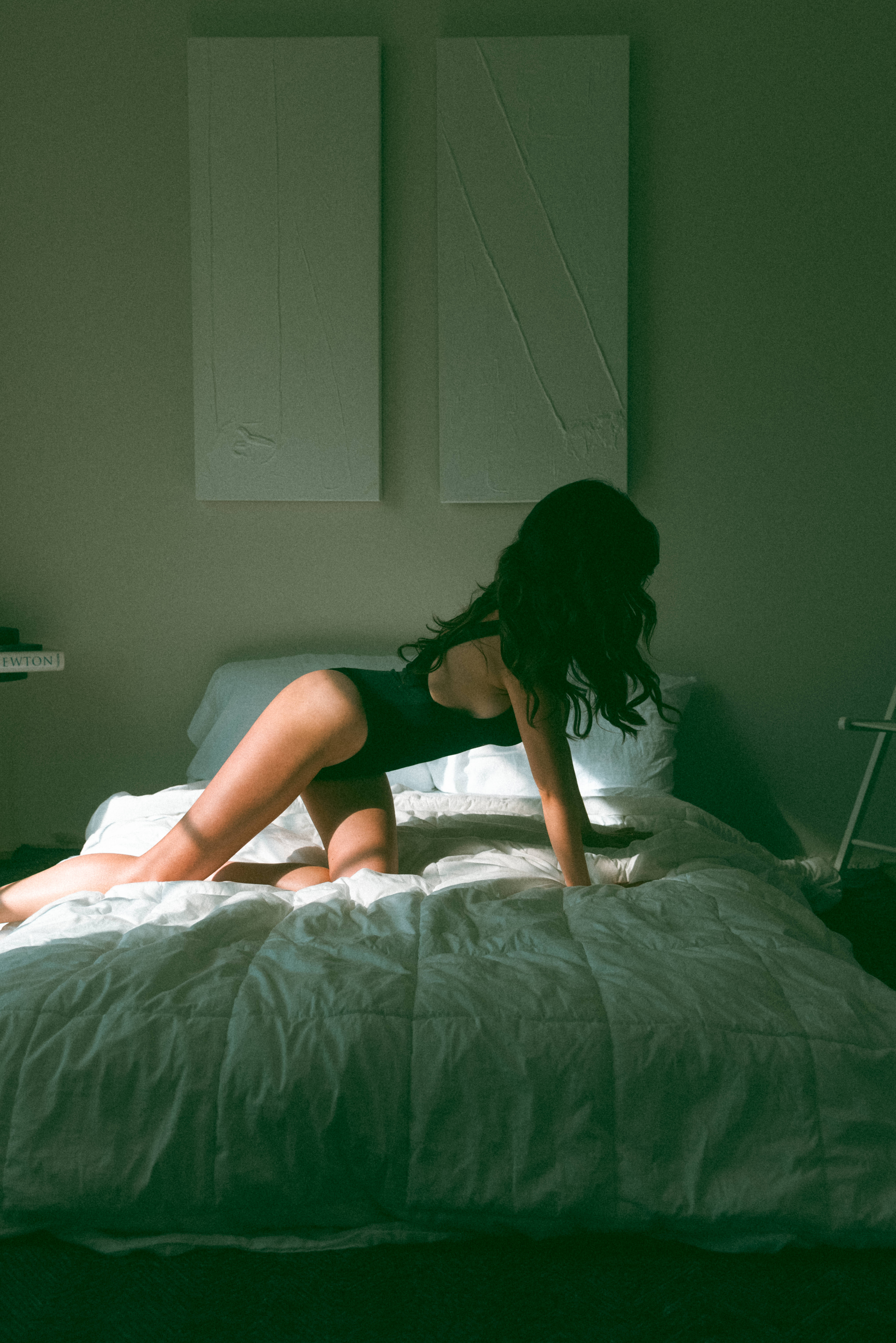 a woman in a one piece on her hands and knees on a bed with light and shadows shining onto her during a boudoir session