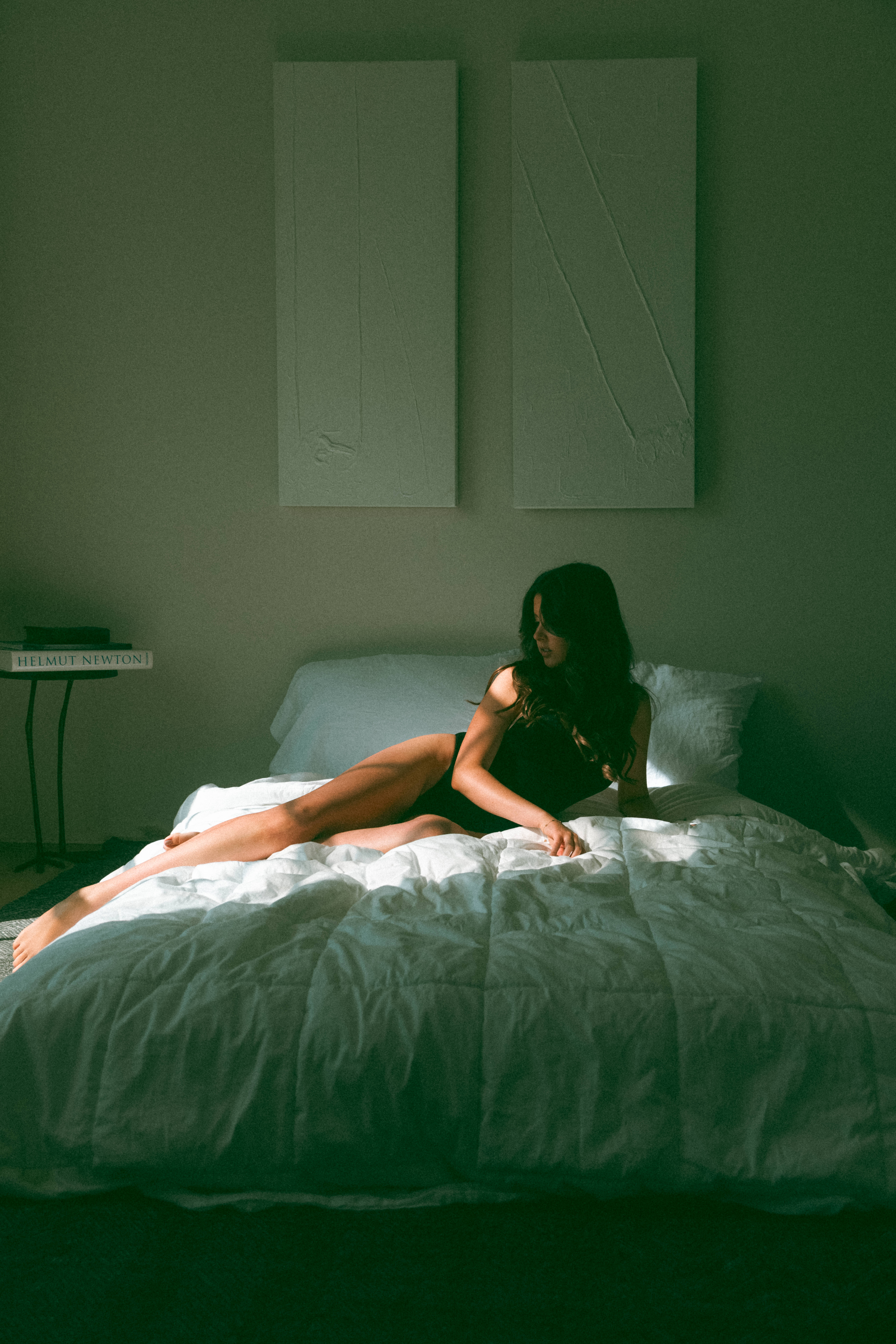 a woman laying on a bed while light and shadows are cast on her body during a boudoir session
