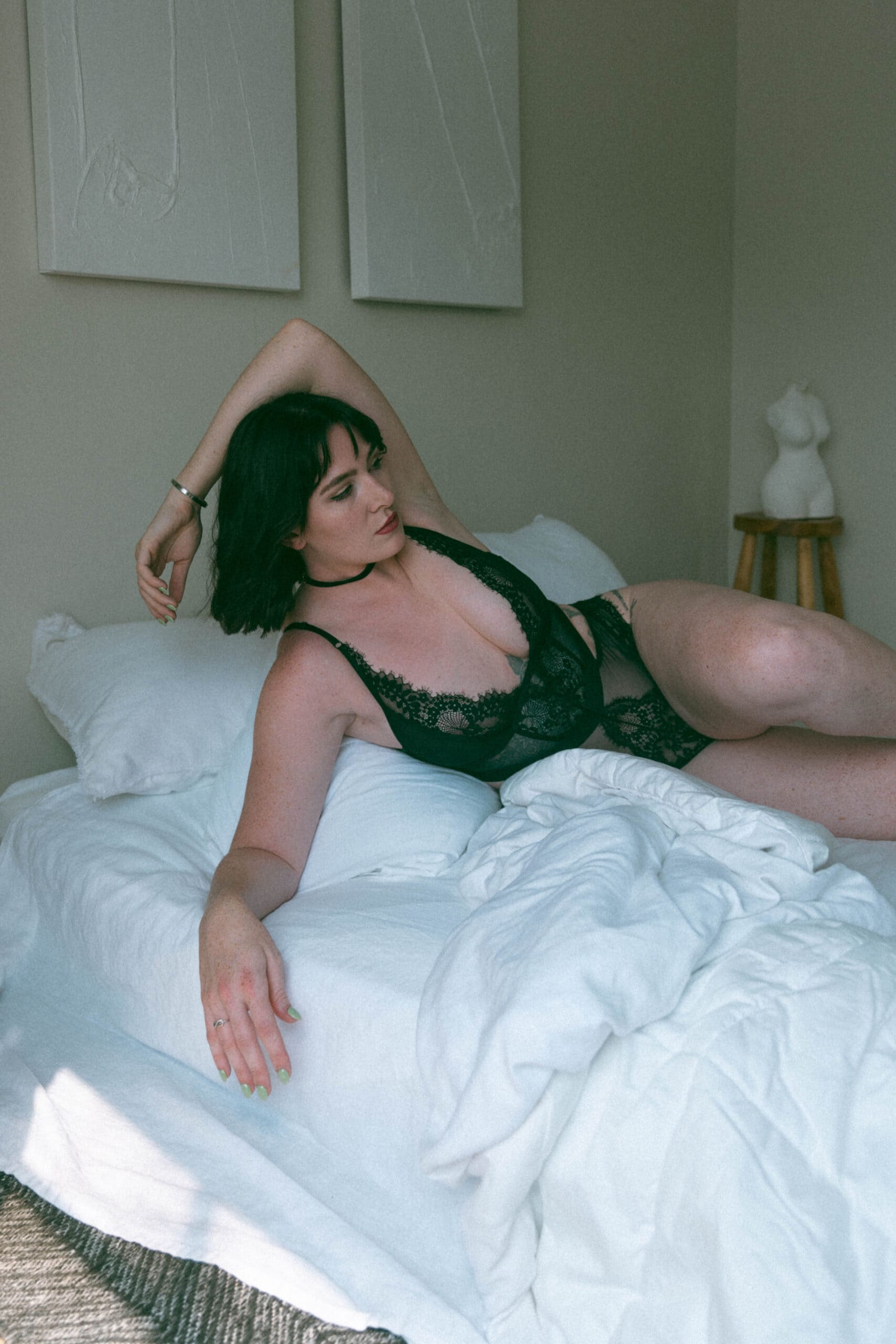 a woman in black intimates laying on a white bed with her arm over her head captured by a Maryland boudoir photographer
