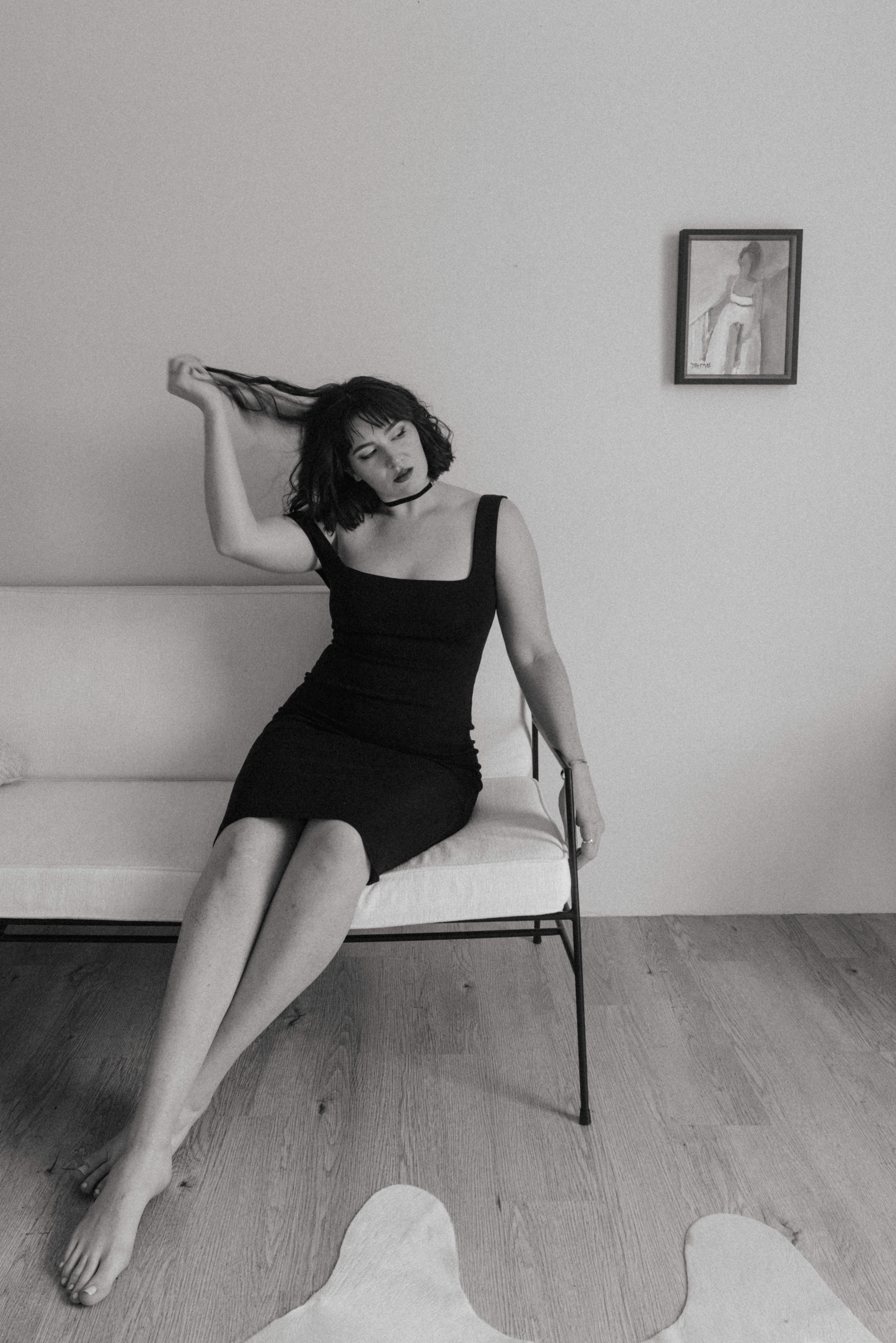 black and white of a woman in a black dress sitting on a couch playing with her hair