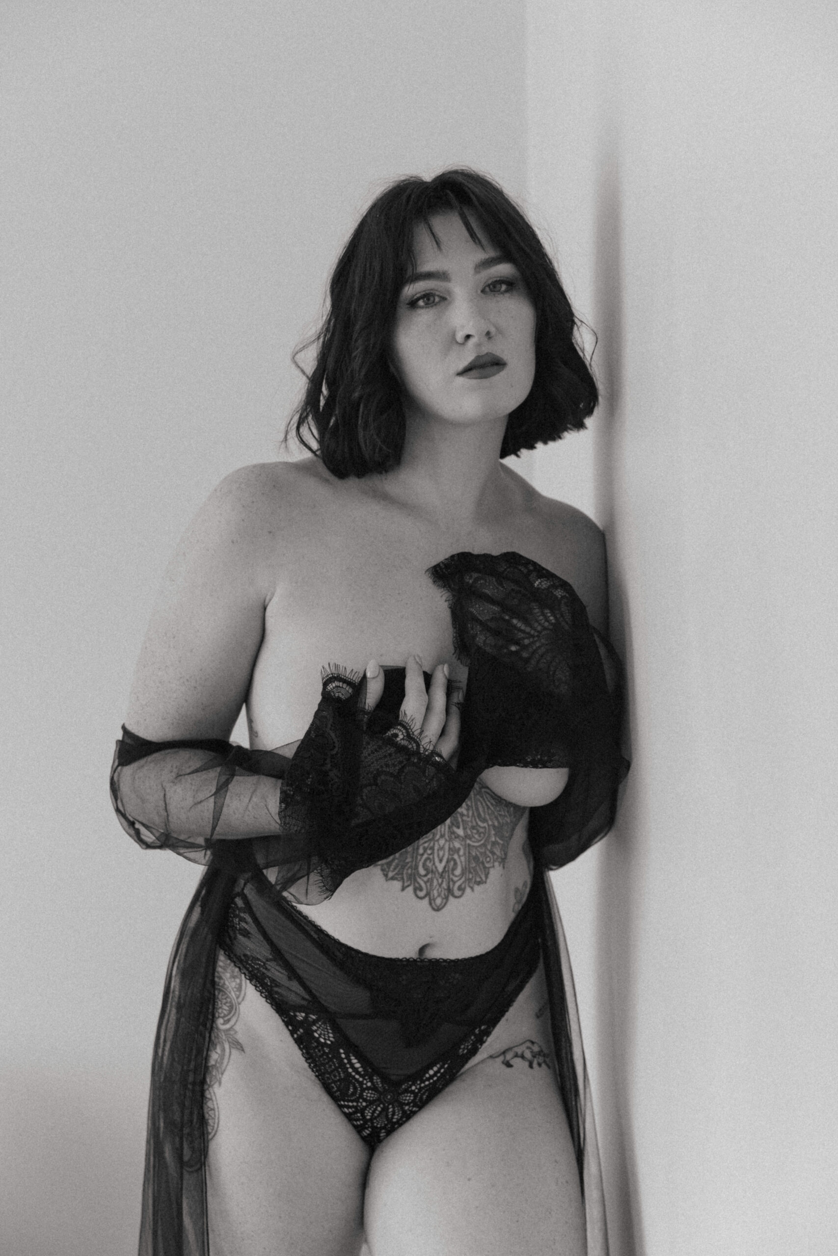 a topless woman with a sheer robe on her arms, leaning against the wall looking at the camera captured by a Maryland boudoir photographer