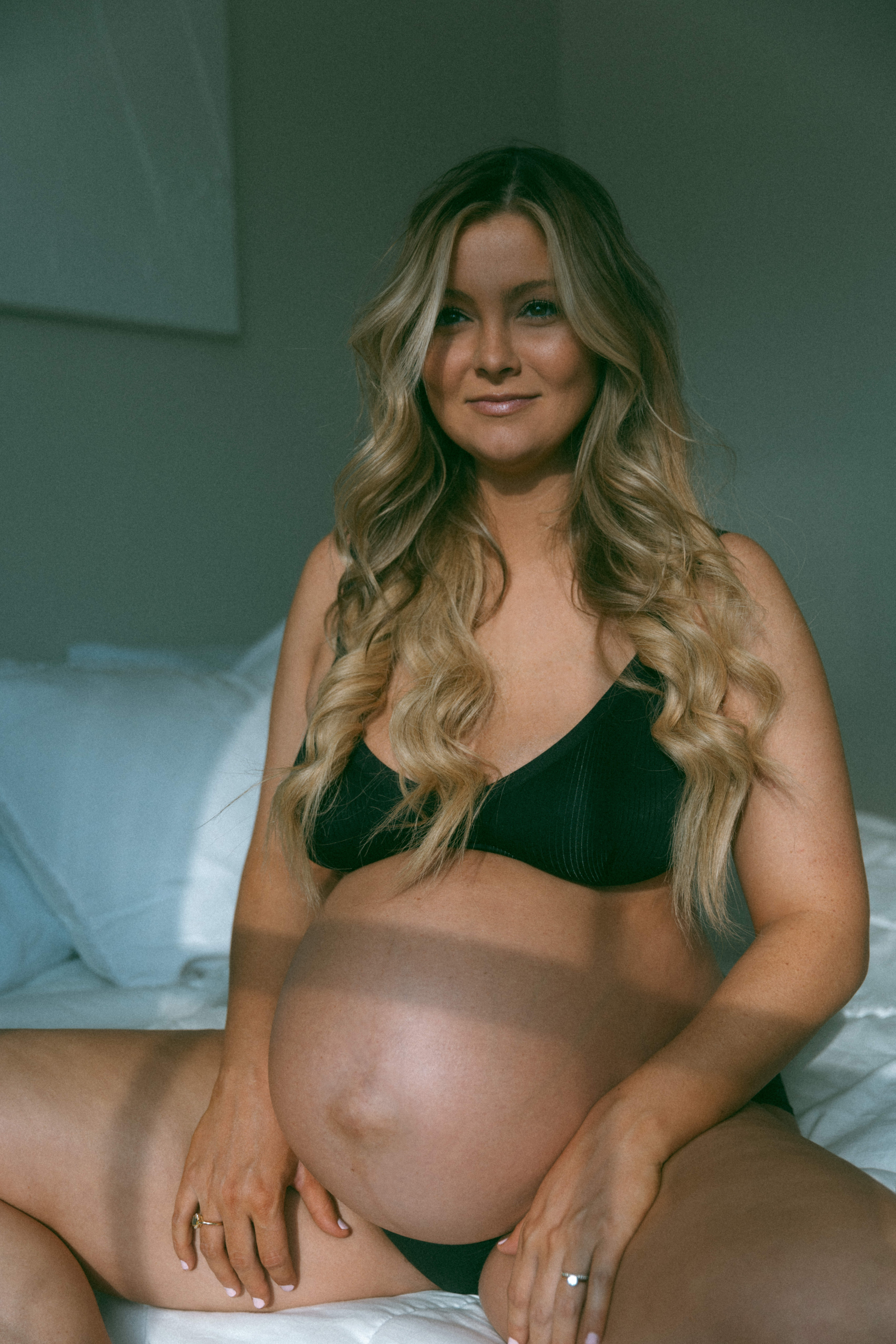 pregnant woman in black intimates sitting on a bed 