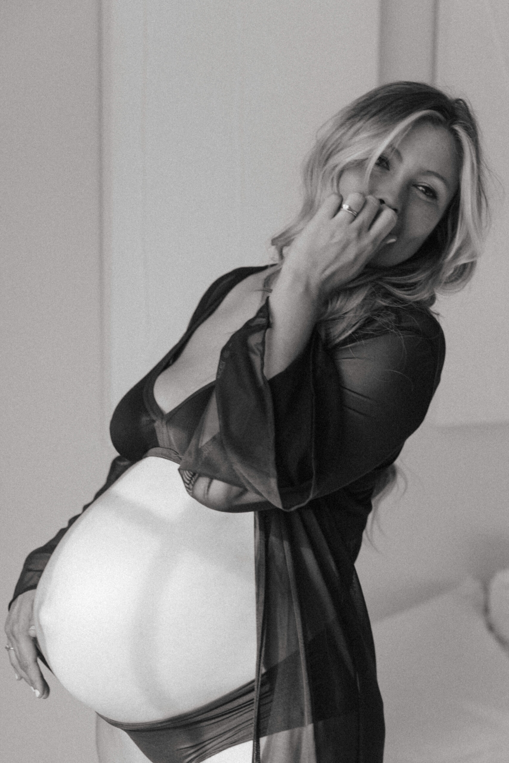 pregnant woman standing in black intimates and a sheer robe 