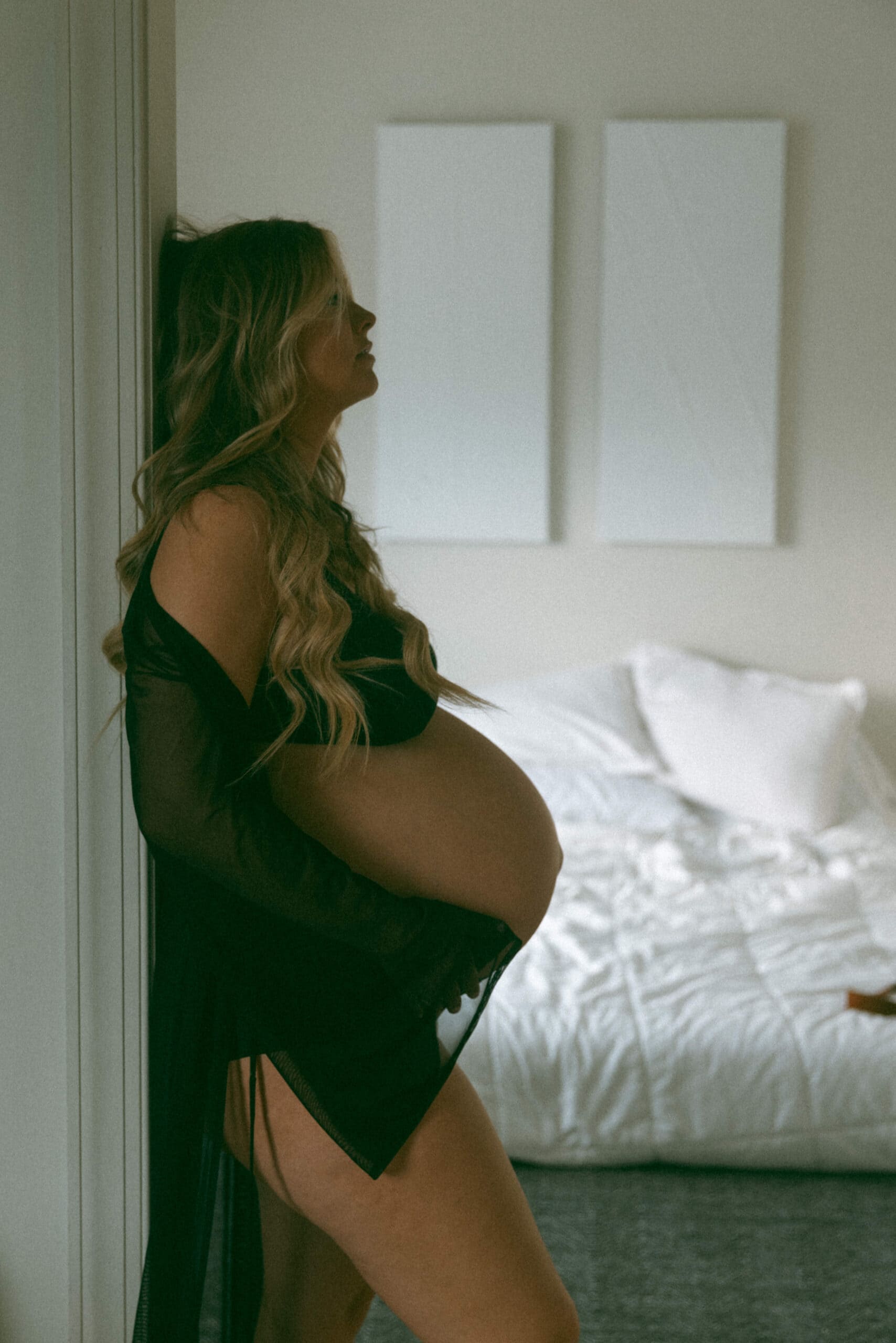 woman standing against a door frame holding her pregnant belly