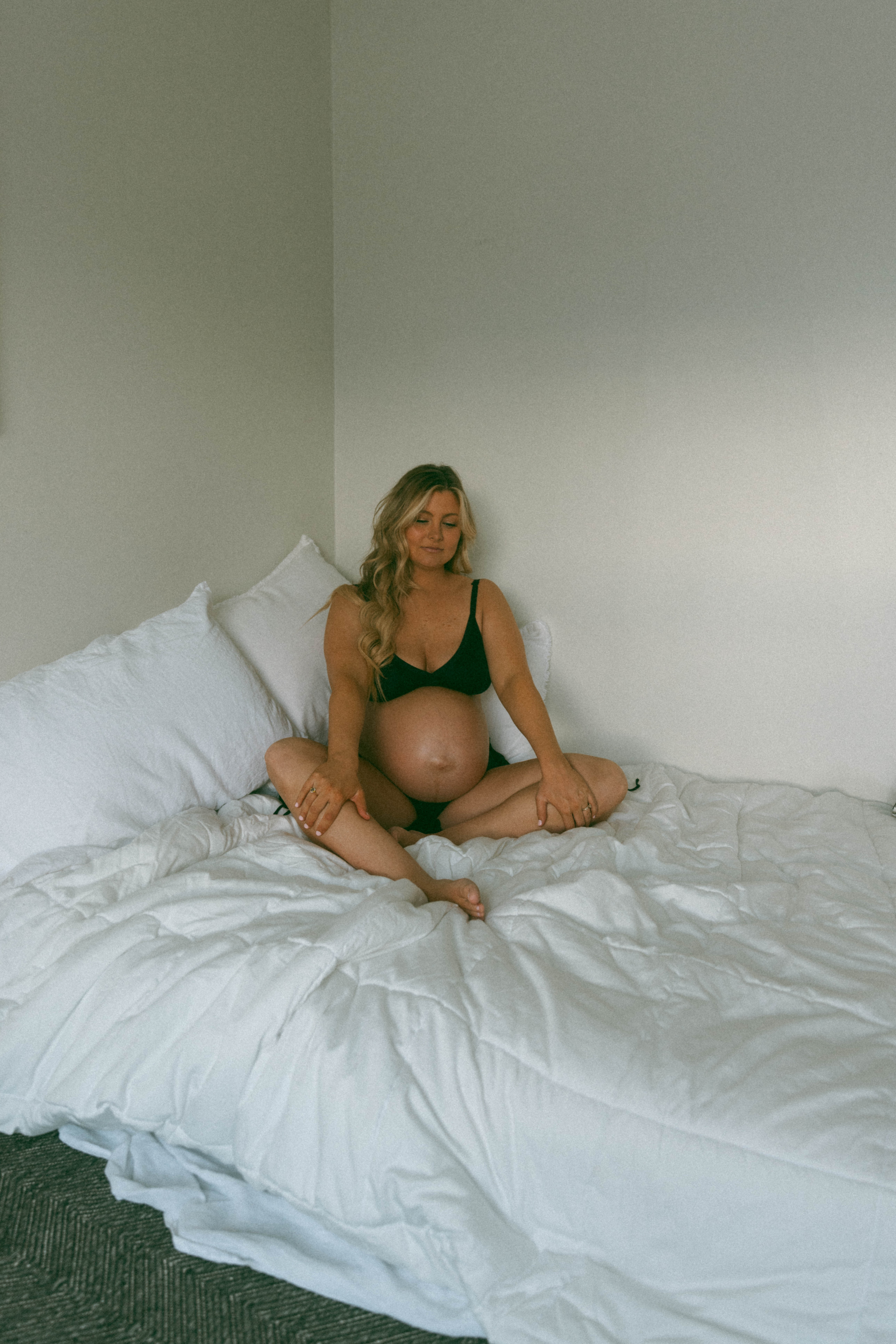 editorial maternity shoot with the woman sitting on a bed wearing black intimates 