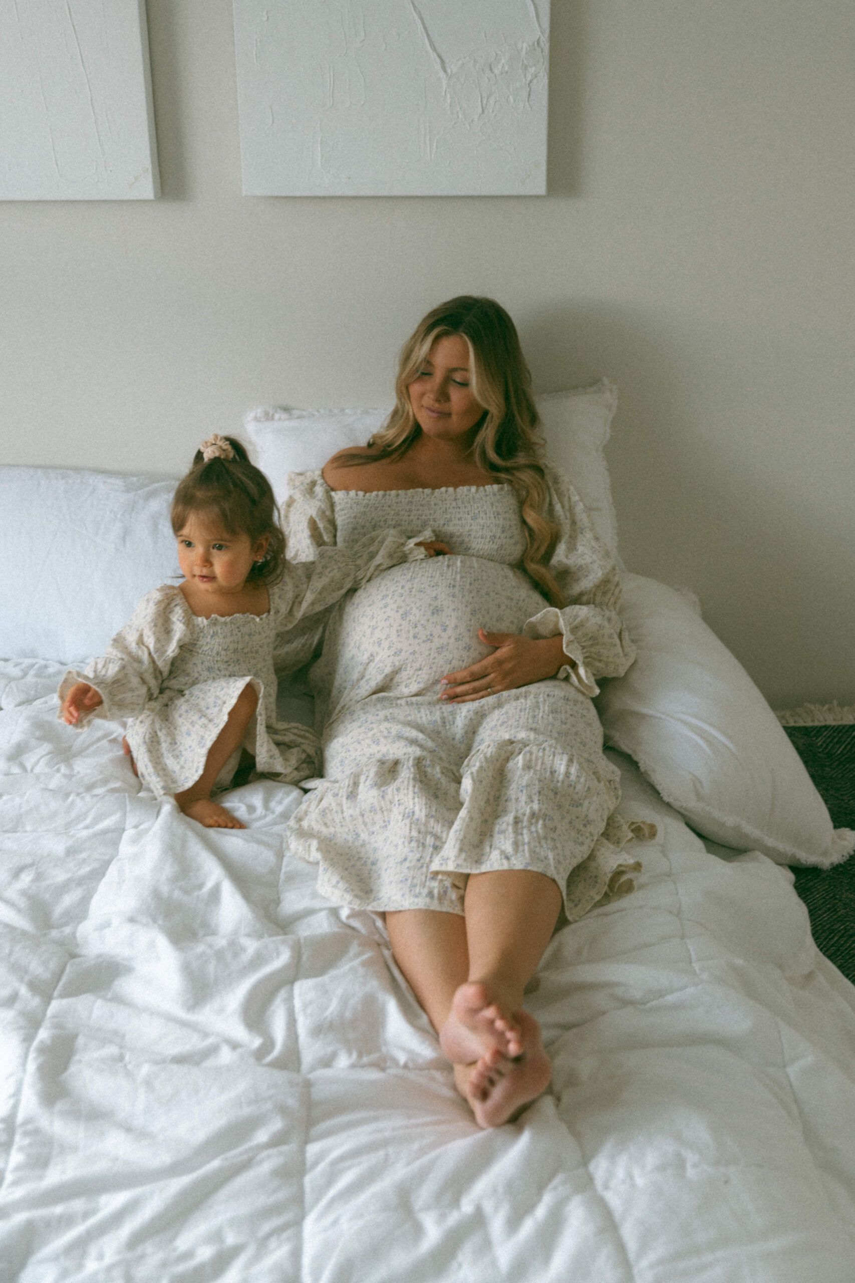 pregnant mother and daughter sitting in a bed together during a studio maternity photoshoot
