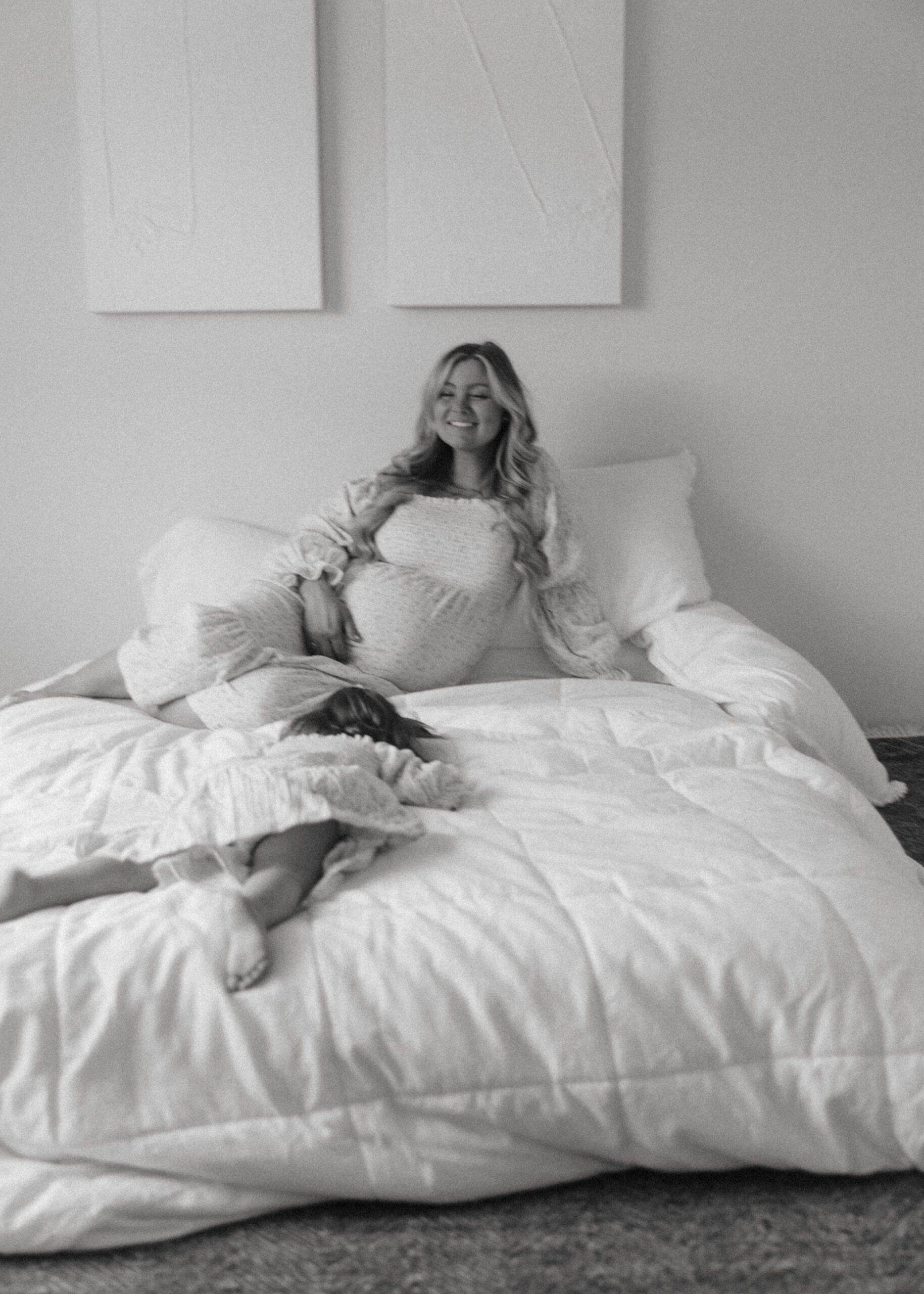 mother and daughter on a bed together laughing during a studio maternity photoshoot