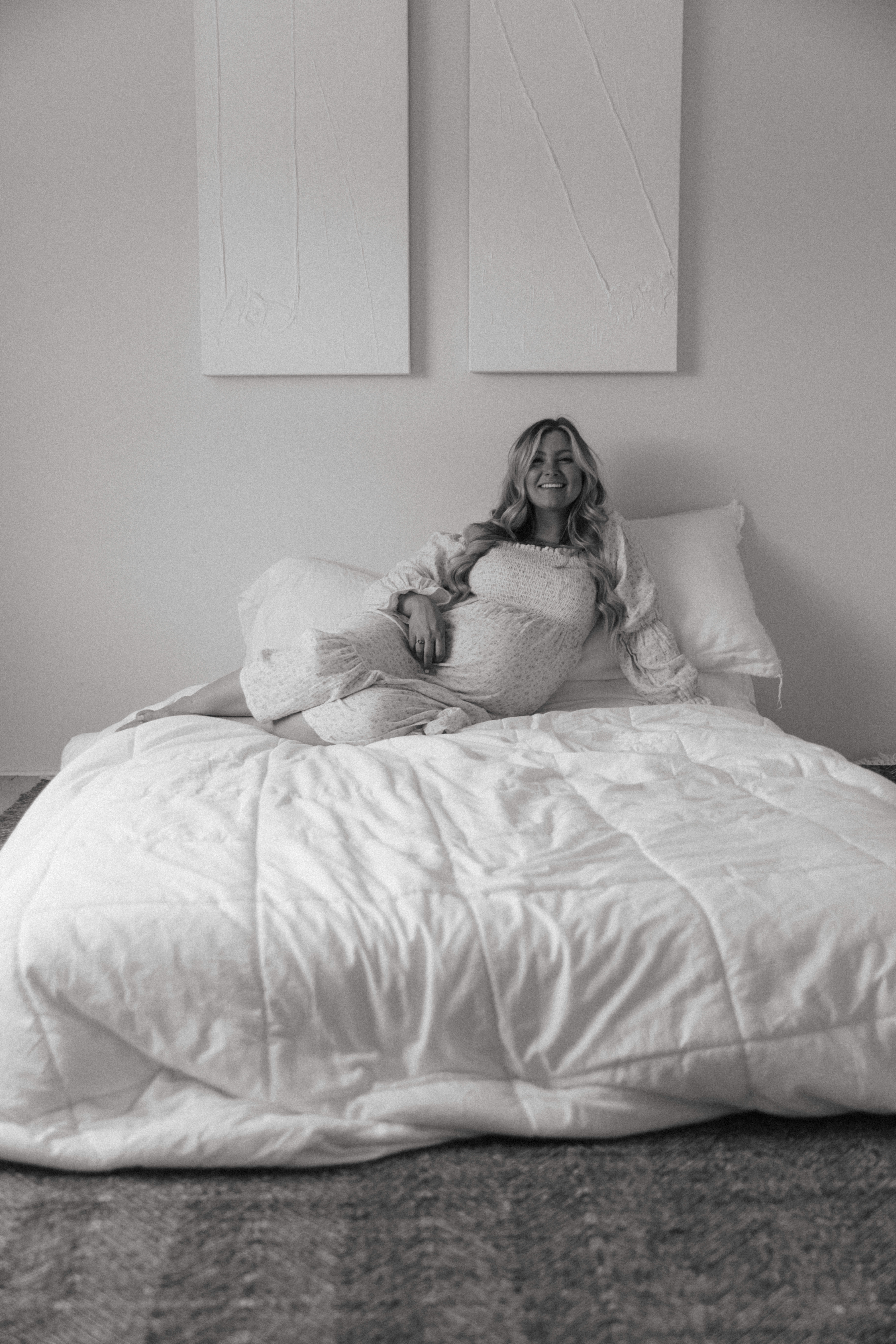pregnant woman laying and smiling on a bed during a studio maternity photoshoot