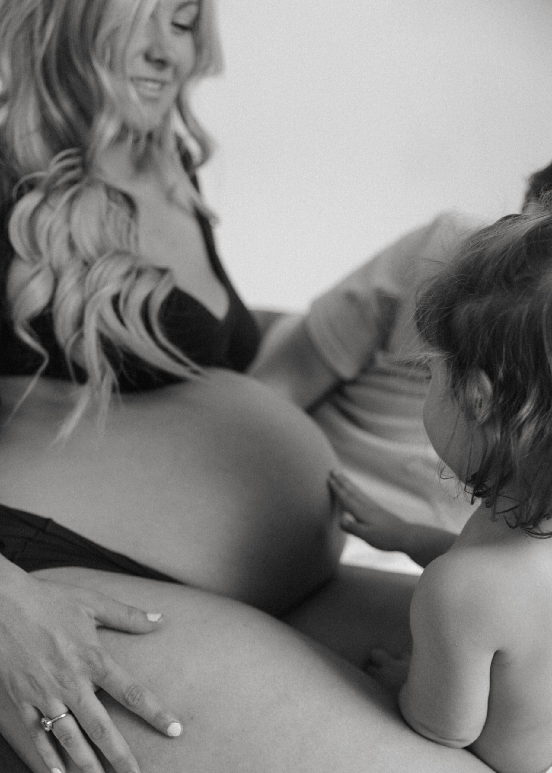 toddler feeling mom's pregnant belly during a studio maternity photoshoot