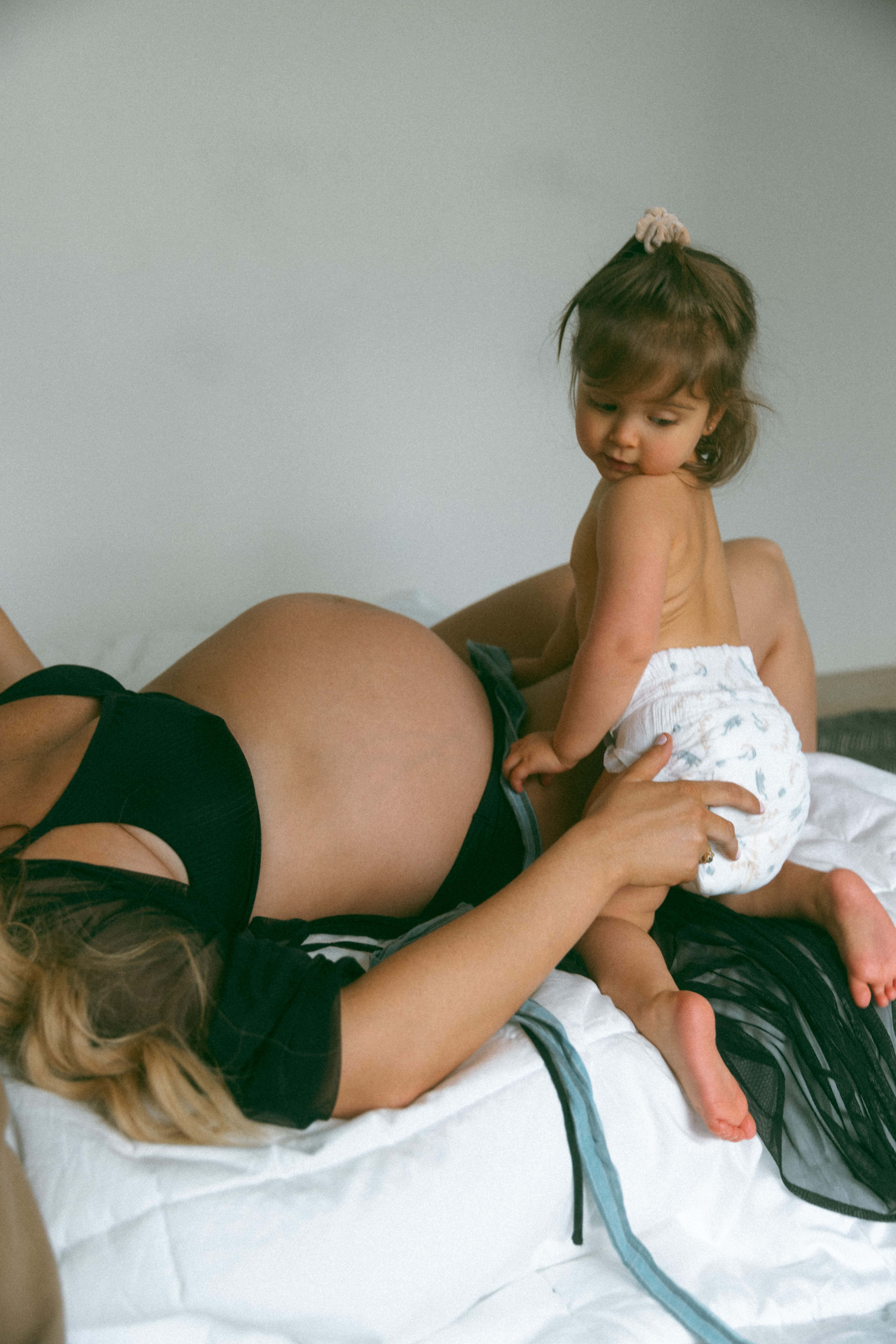 mother laying on the bed and toddler kneeling beside her during a studio maternity photoshoot
