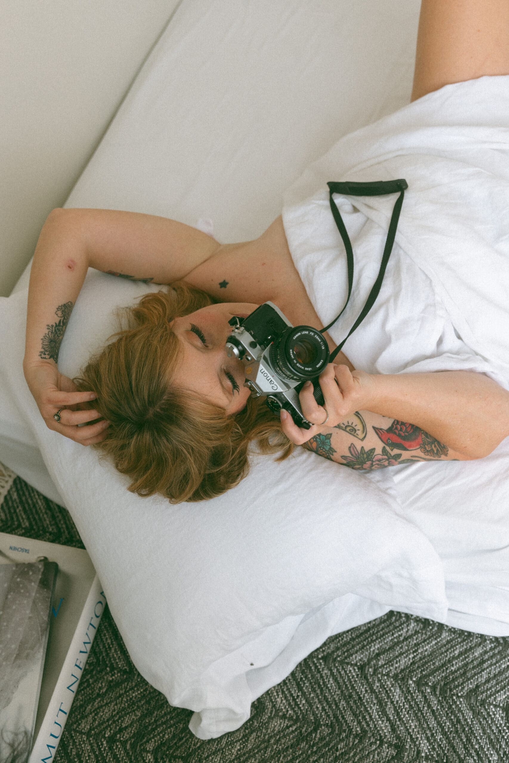 a woman laying in a bed with a camera to her face during a boudoir photo session in Maryland