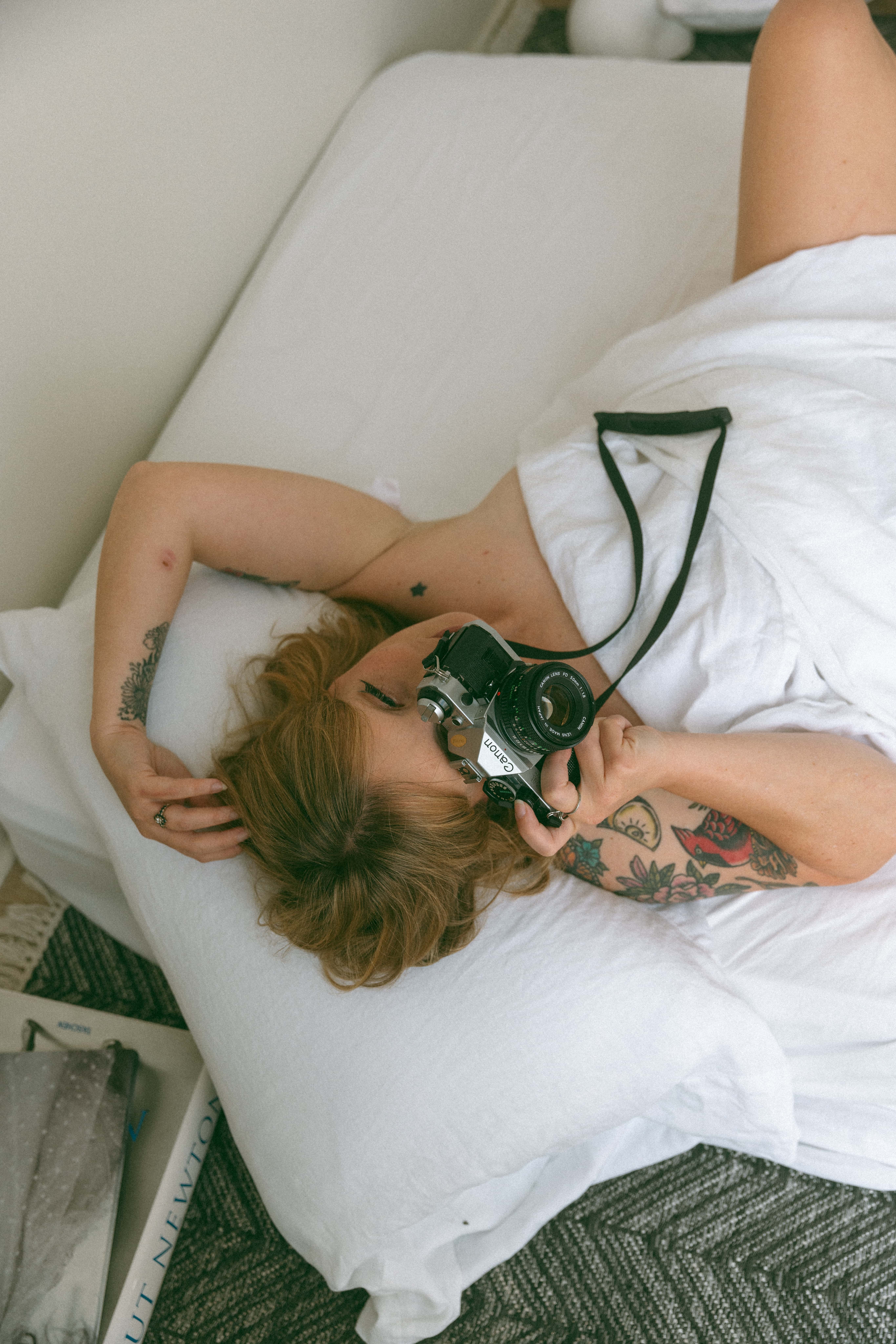 a woman laying naked in bed with a camera to her face 