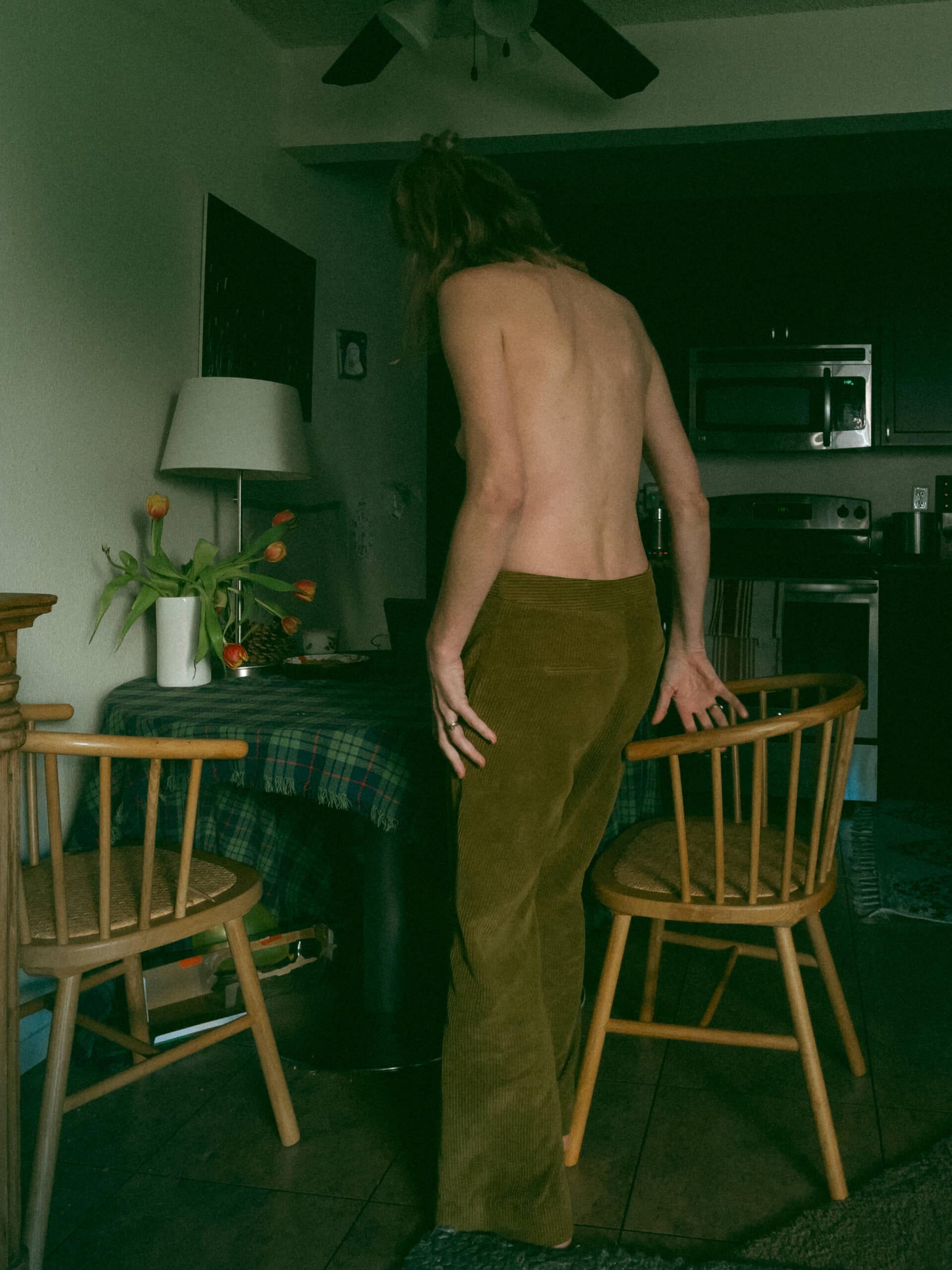 a topless woman standing by a kitchen table 
