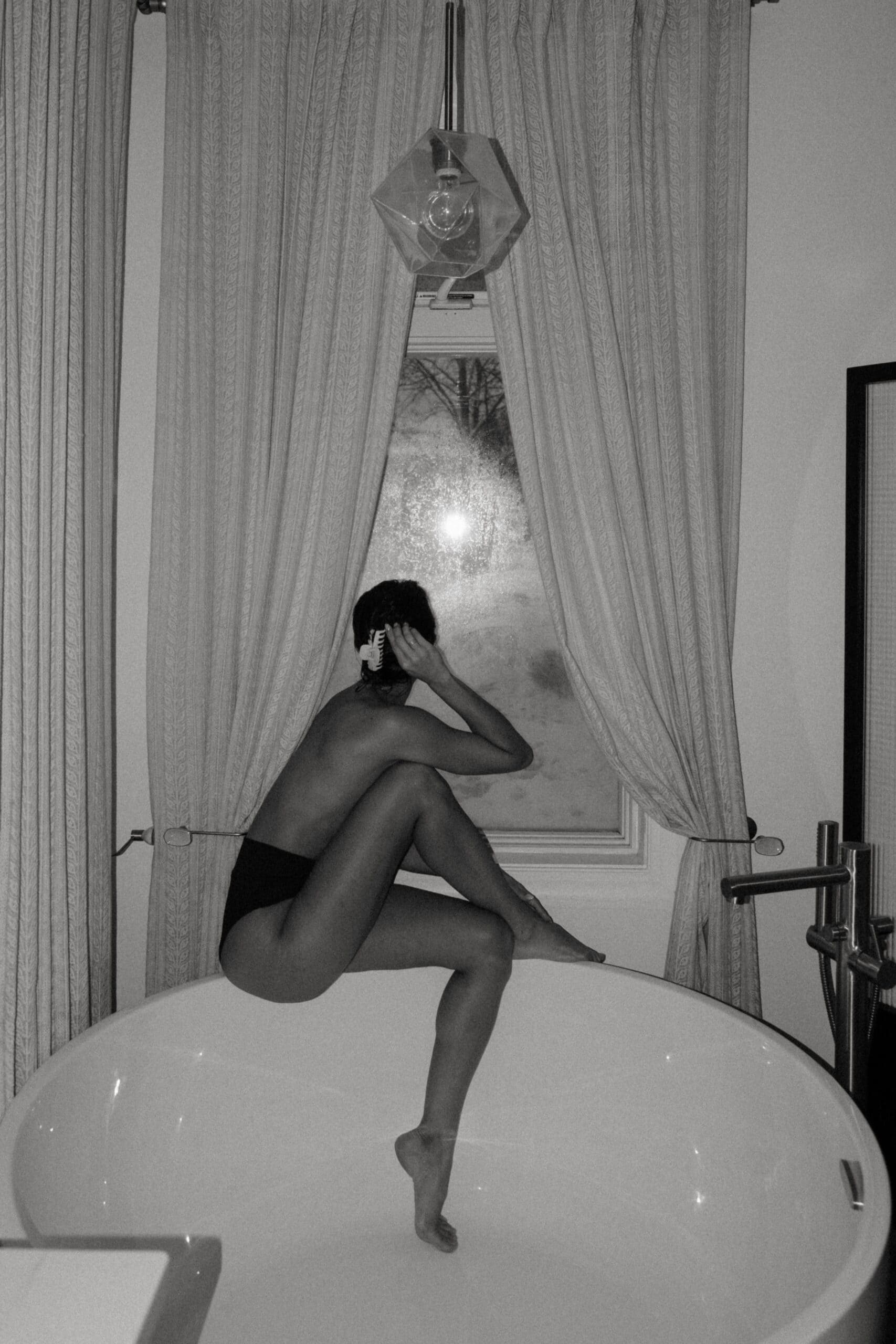 a woman sitting on the tub looking out the window 