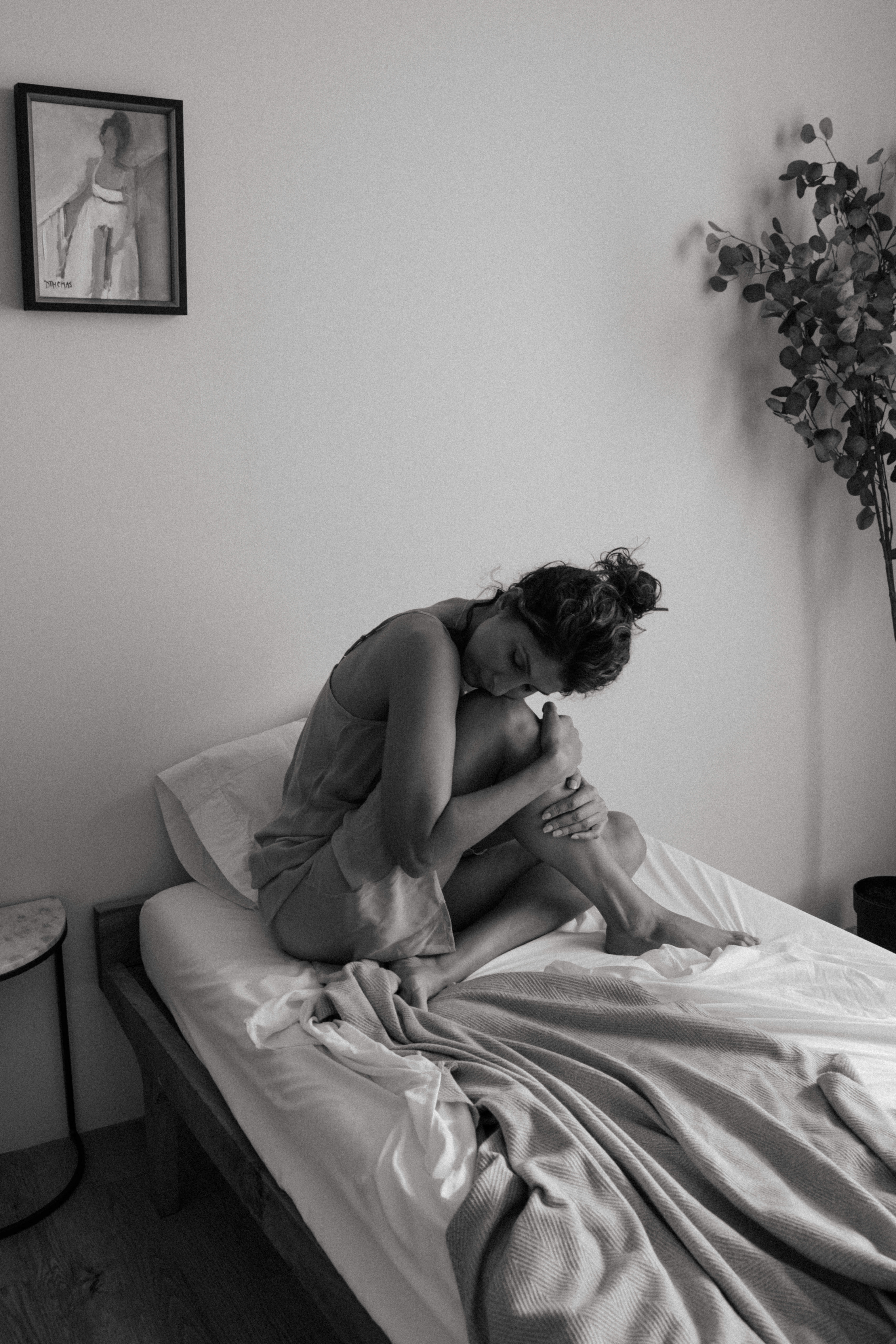 a woman curled into her knees sitting on a bed 