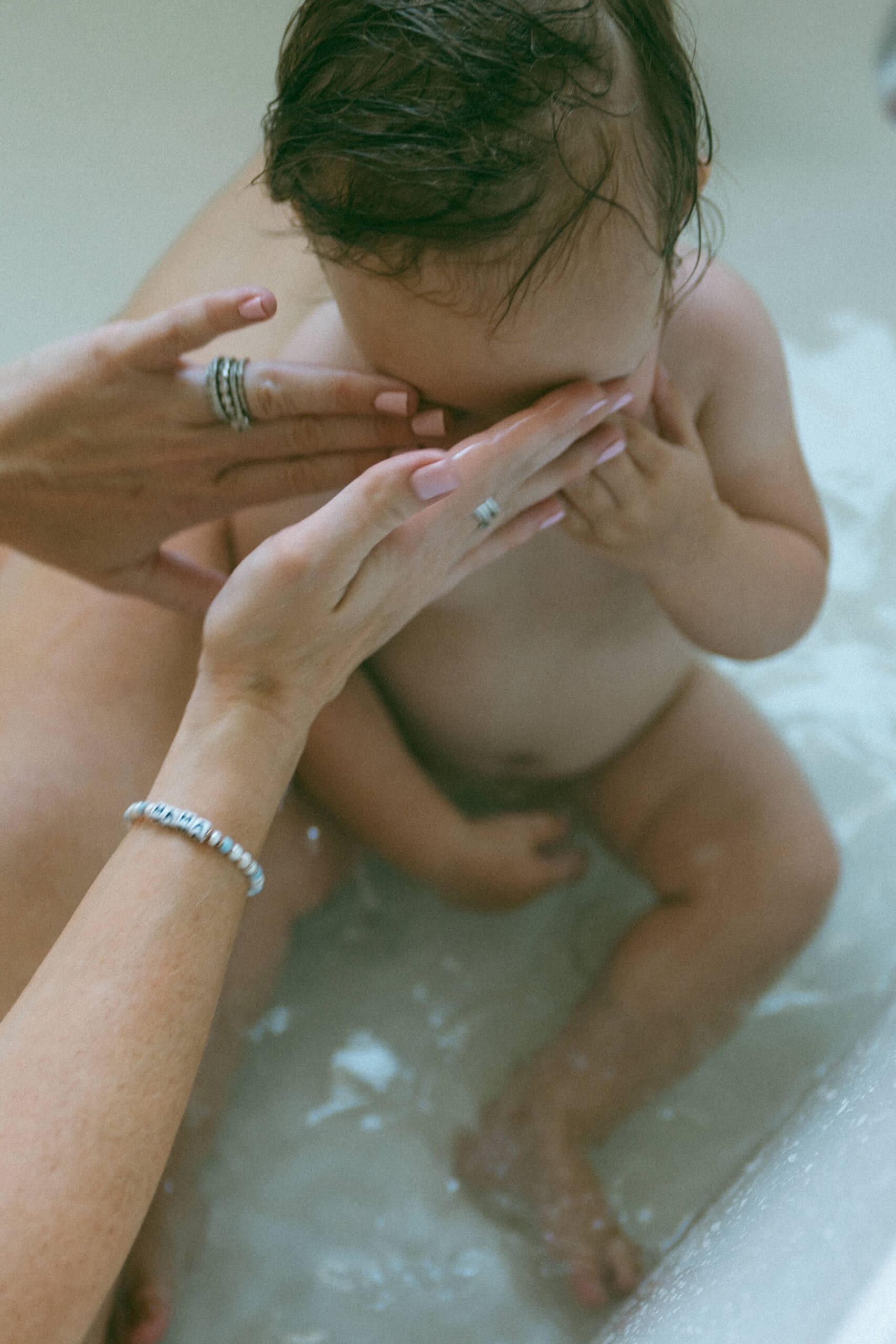 mama covering baby's eyes in the bath captured by a motherhood photographer 