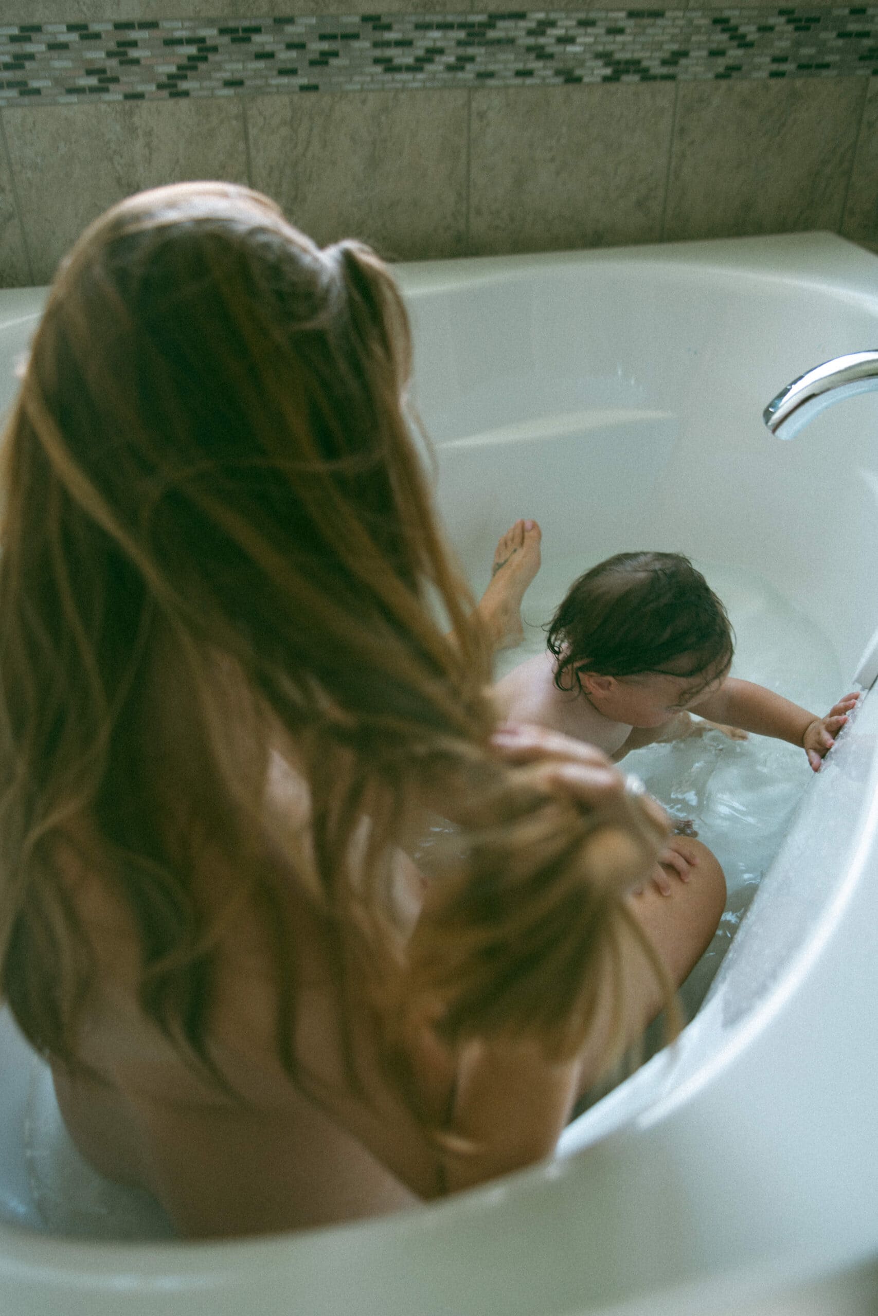raw motherhood photoshoot of mama and baby in the bathtub together 