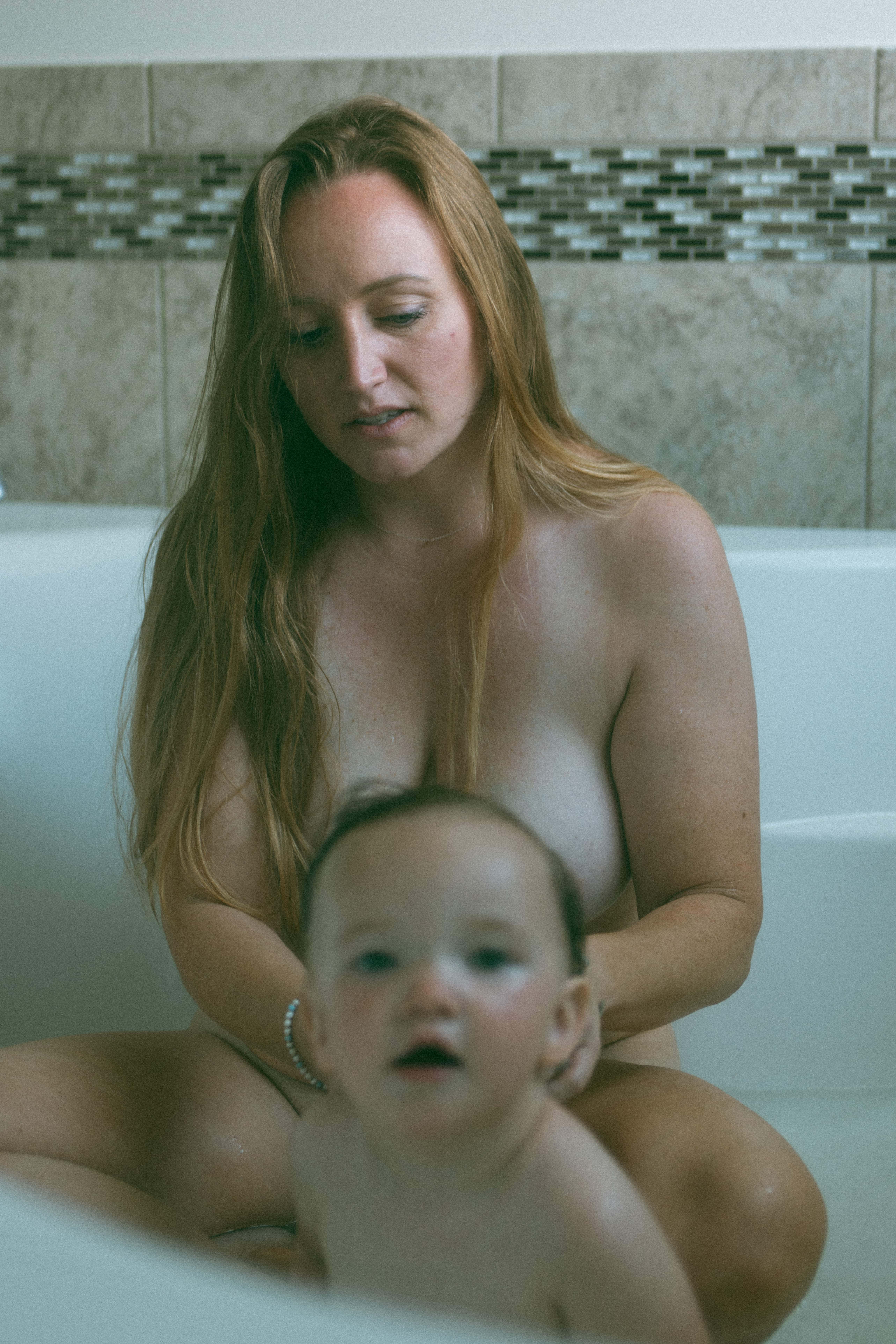 mama is sitting looking at her baby in the tub and baby is looking at the camera 