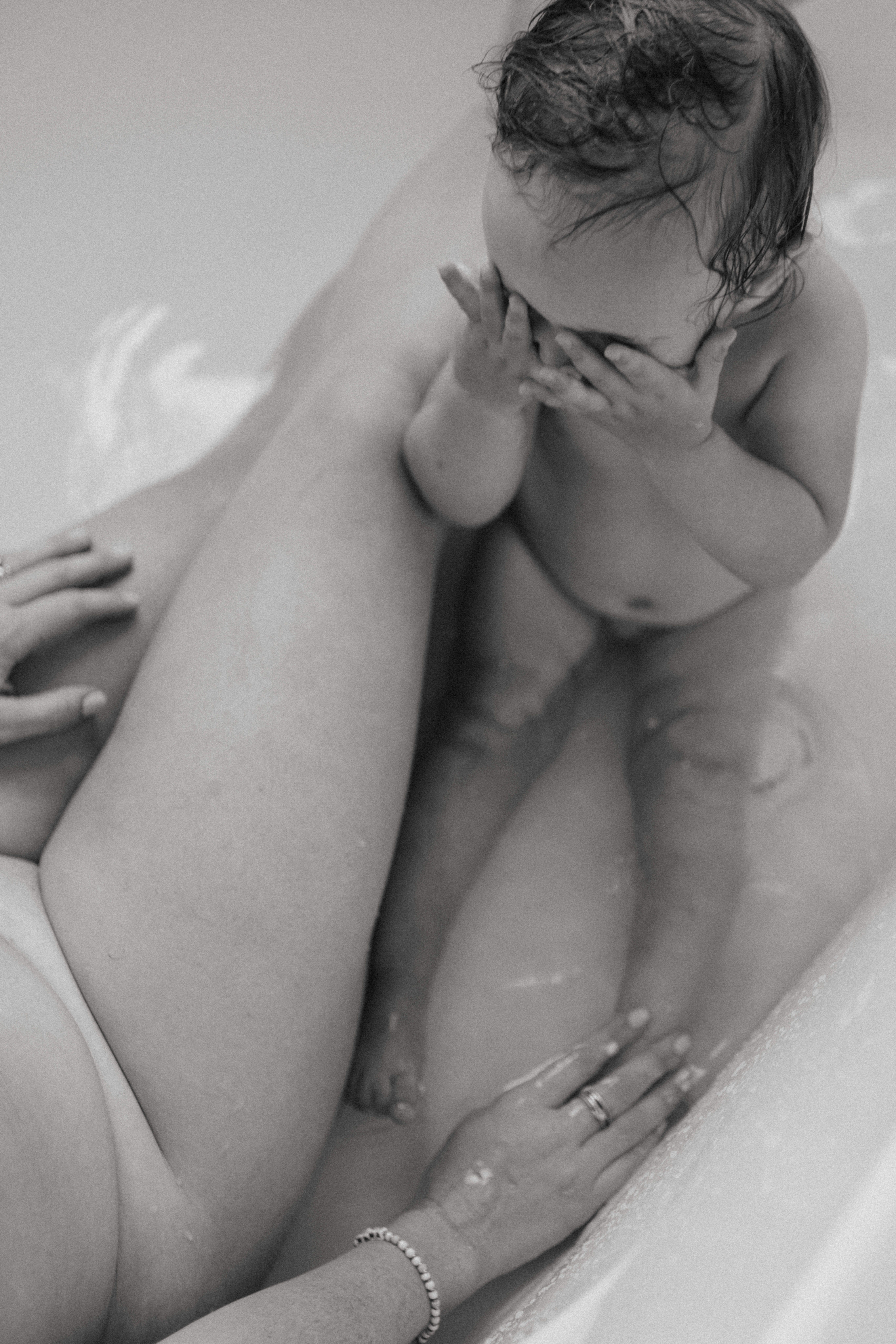 mother and baby taking a bath and baby covering her eyes