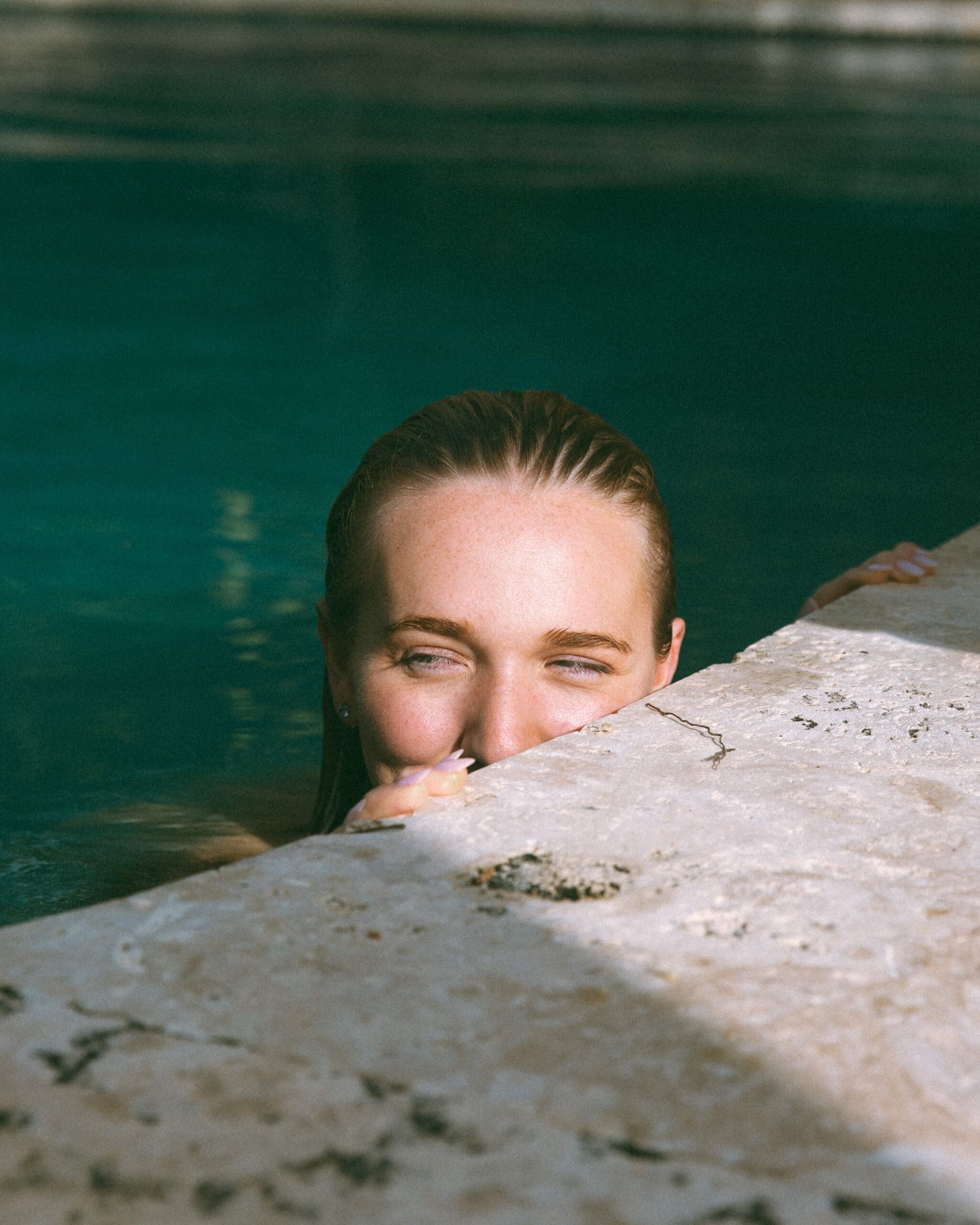 portrait of a woman smiling over the ledge while in a pool 